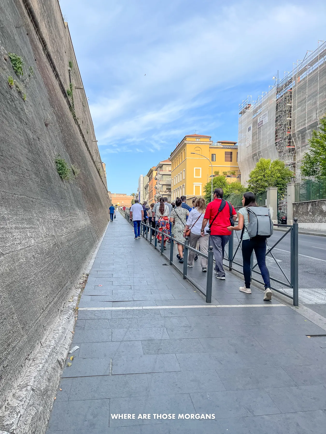 City wall with two pedestrian walkways separated by a black railed fence marking lines for entrance to an attraction