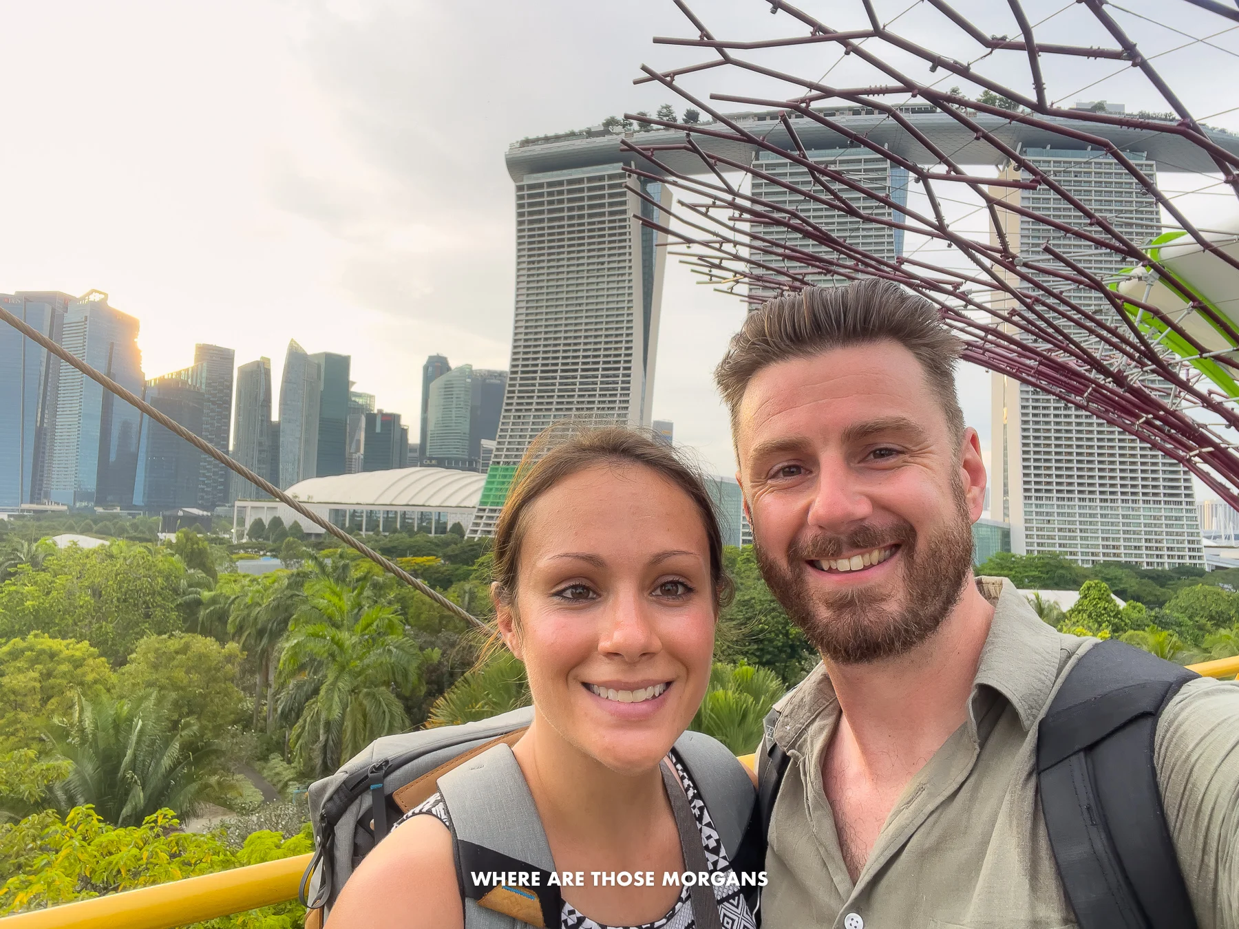 Mark and Kristen from Where Are Those Morgans taking a selfie in Singapore with Marina Bay Sands hotel and city skyscrapers behind as the sun is setting