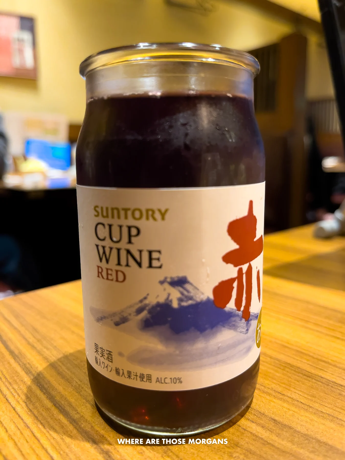 Small glass filled with wine and a white label with the words Suntory cup wine red  on a table