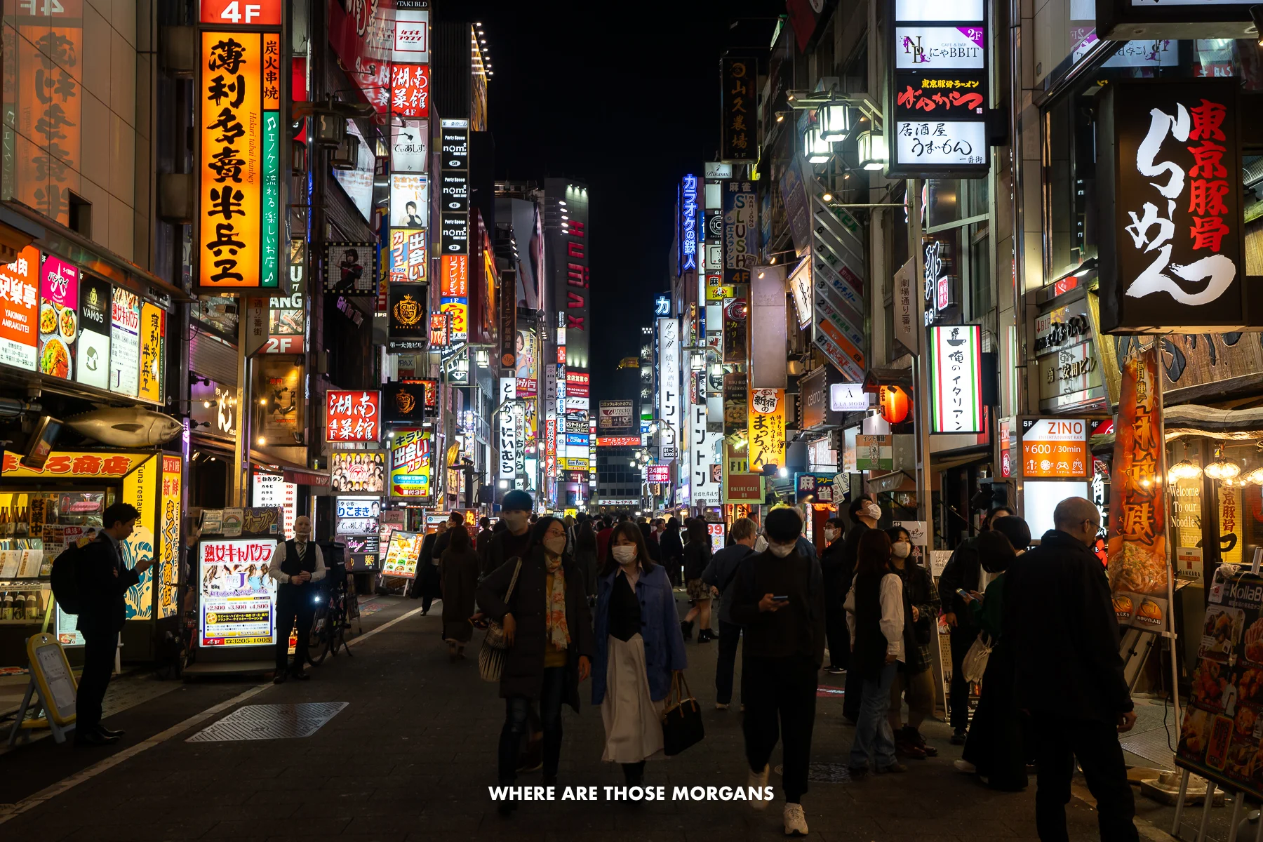 Crowds of people walking down a street in Tokyo at night with neon lights on buildings lighting the street