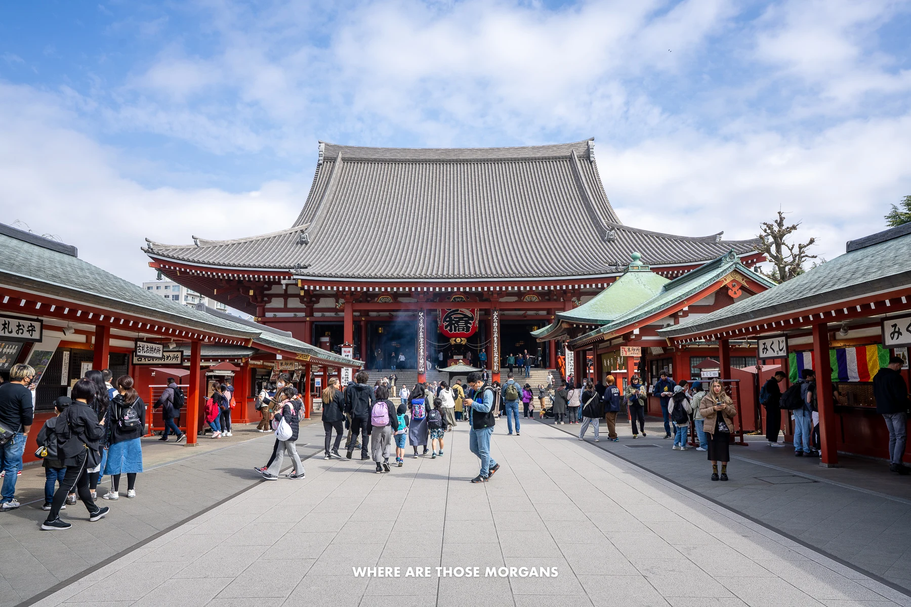 Tourists and locals walking around a Buddhist temple complex with red colored buildings under a blue sky