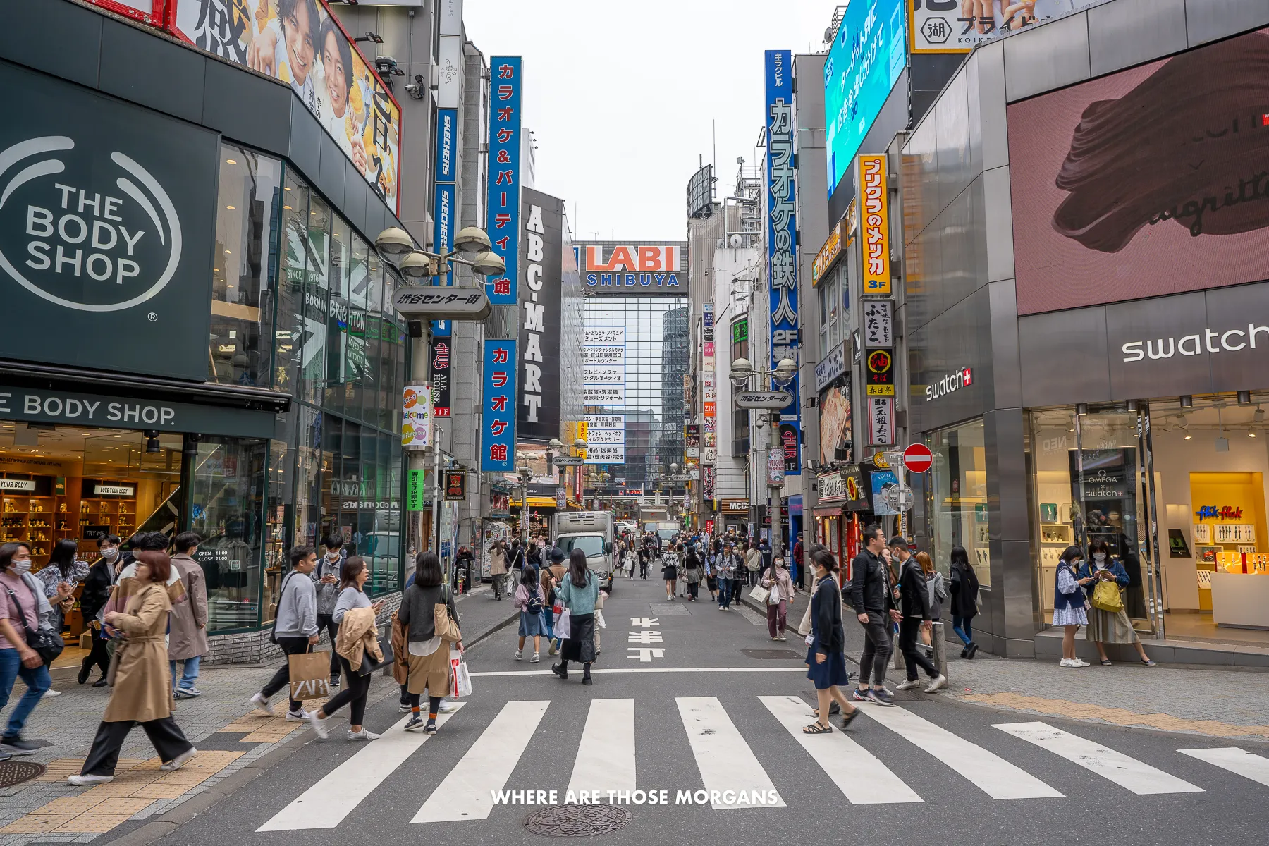 Lots of tourists and locals walking across a pedestrian crossing next to lots of shops and buildings
