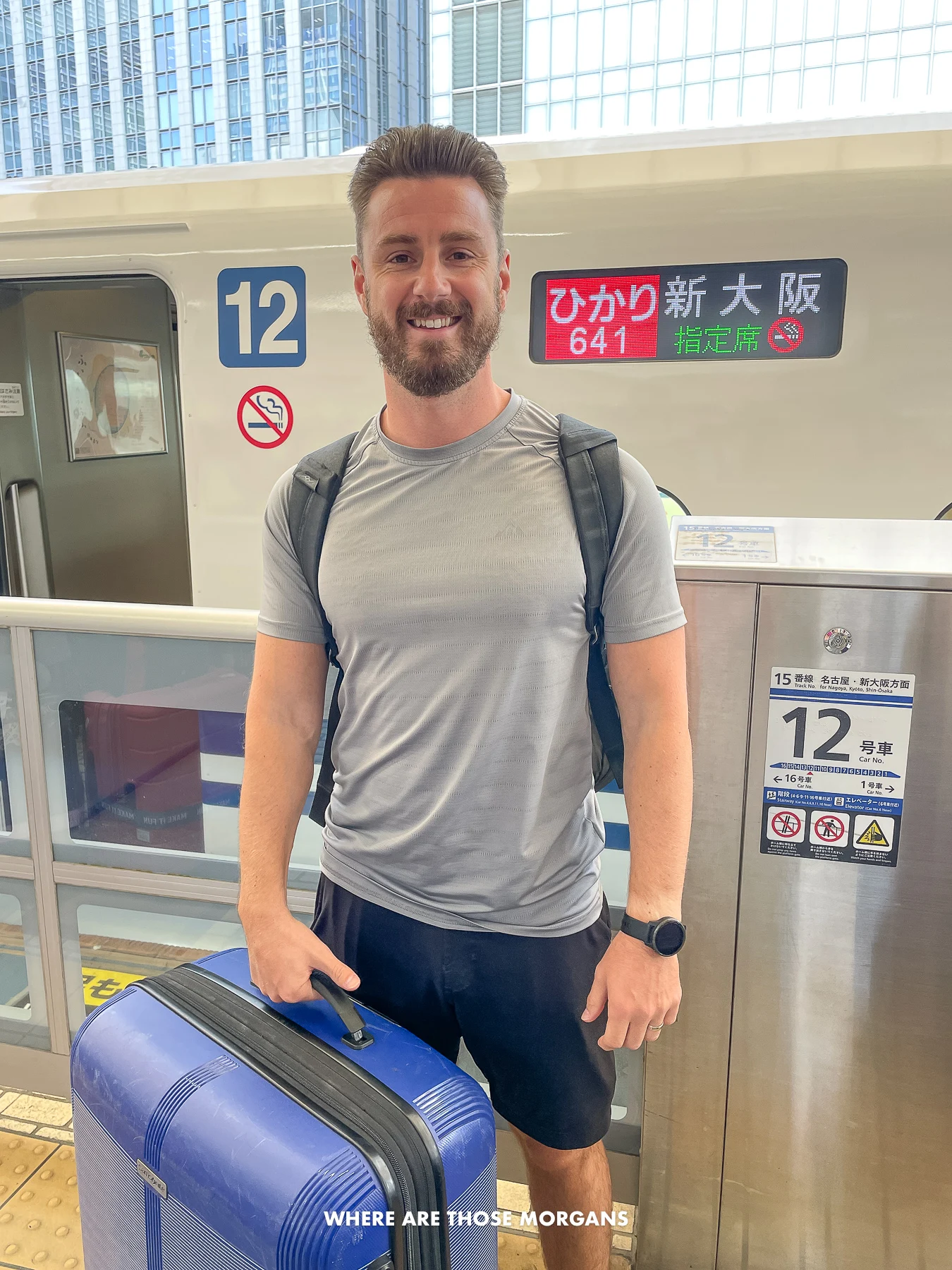 Mark from Where Are Those Morgans holding a blue suitcase outside a bullet train in Japan