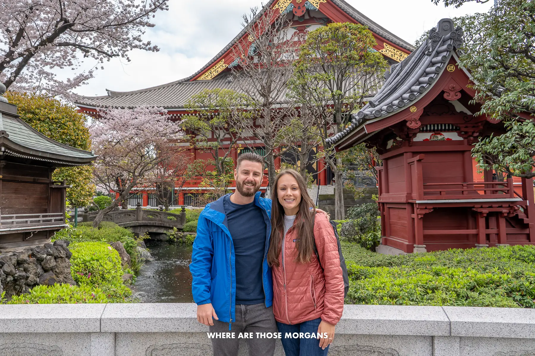 Mark and Kristen from Where Are Those Morgans standing together for a photo with. a low wall, garden and red wooden temples behind in Tokyo Japan