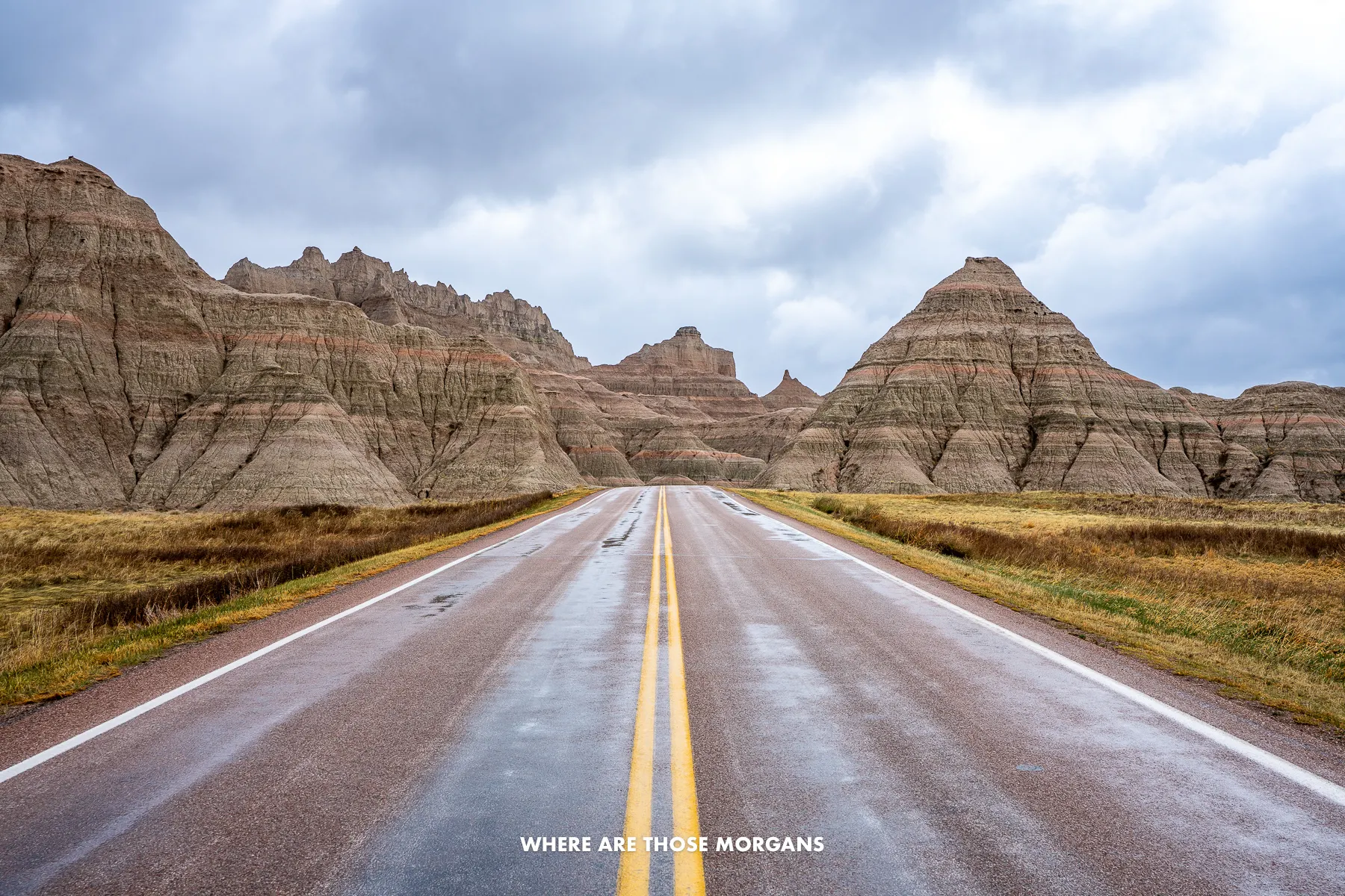 Empty straight road leading through rocky mounds in Badlands SD under a cloudy sky