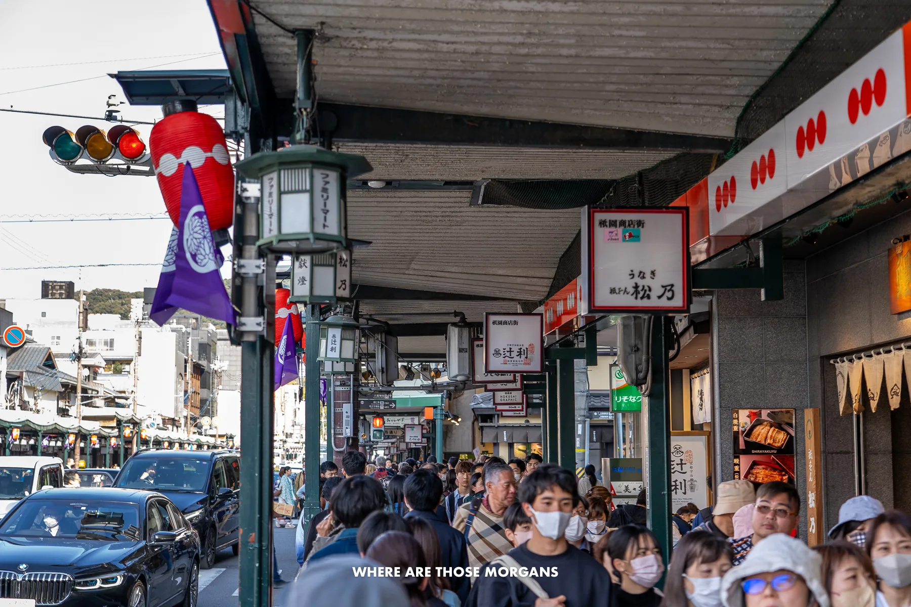 Crowded street in Downtown Kyoto with lots of people on the path and cars on the road