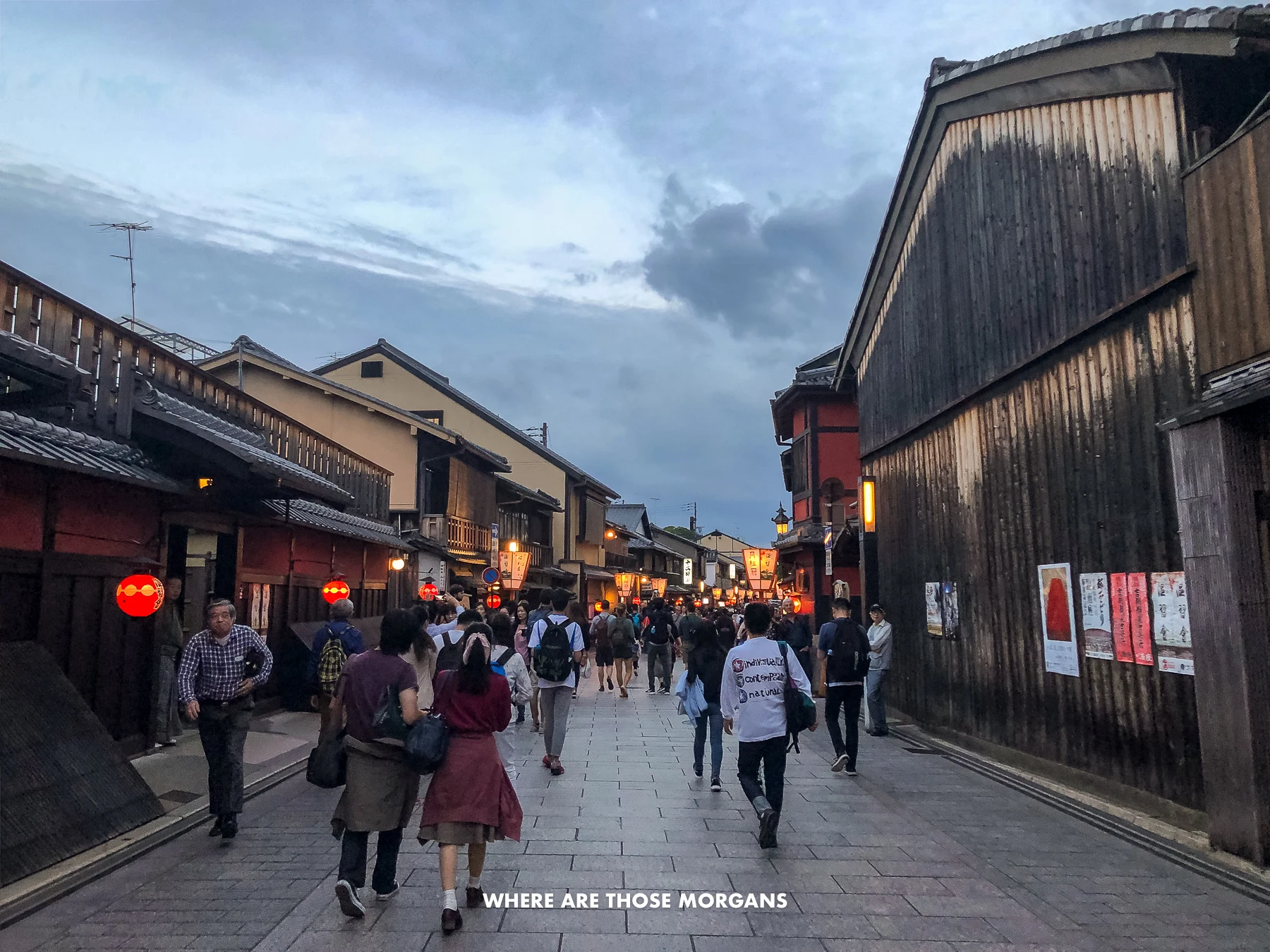People walking down a narrow street flanked by wooden buildings and lanterns in Gion