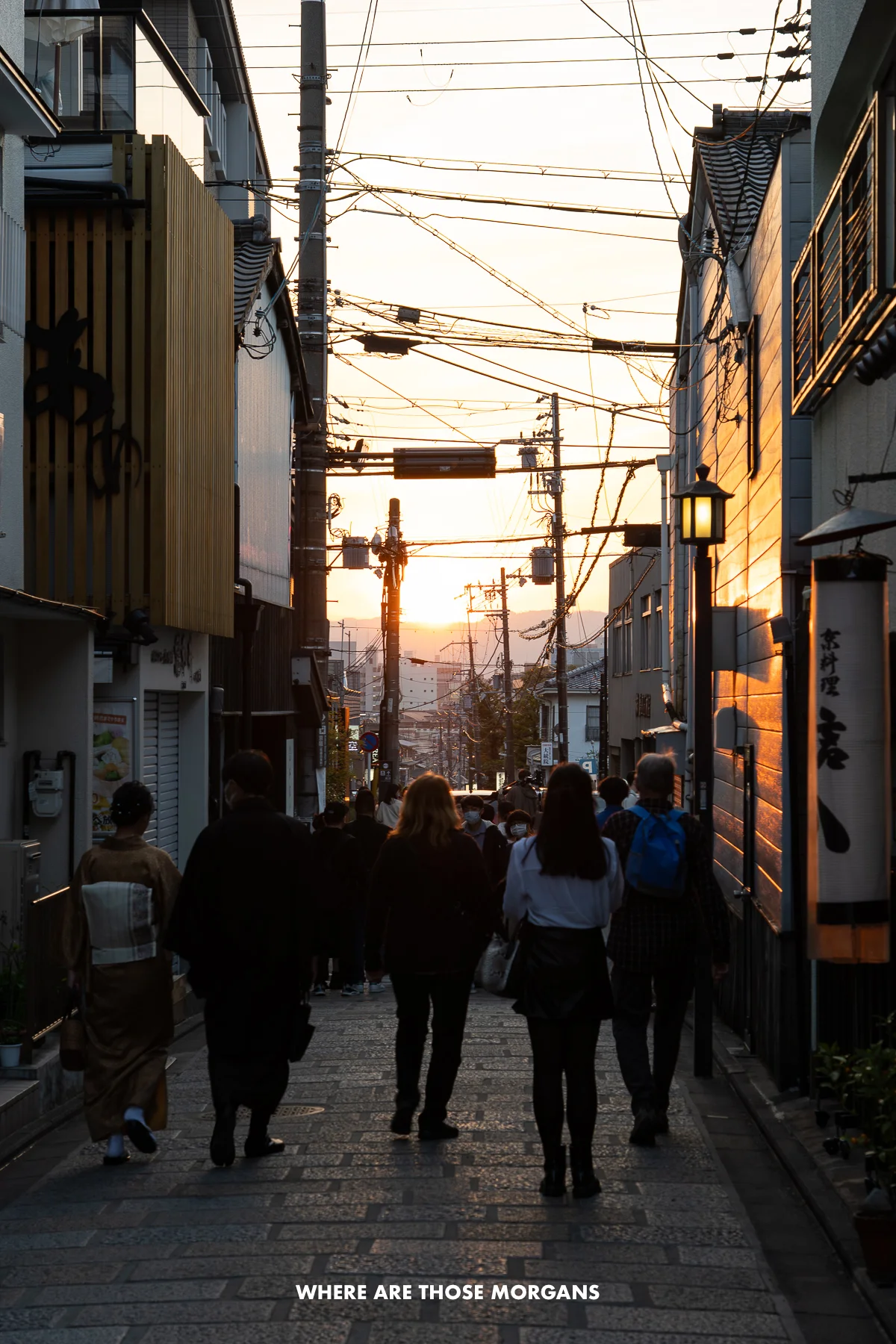 People walking down a narrow street with power lines exposed at sunset
