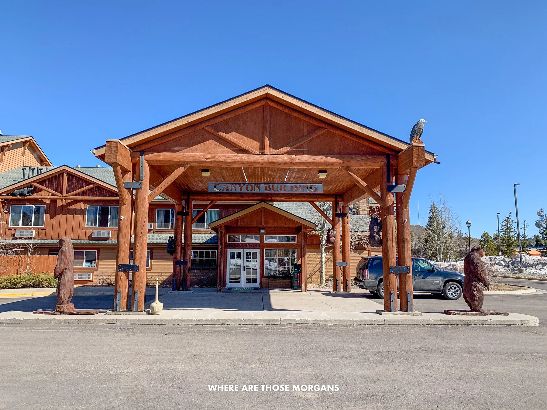 Looking at the entrance to a hotel made of massive wooden beams in West Yellowstone on a clear day with blue sky