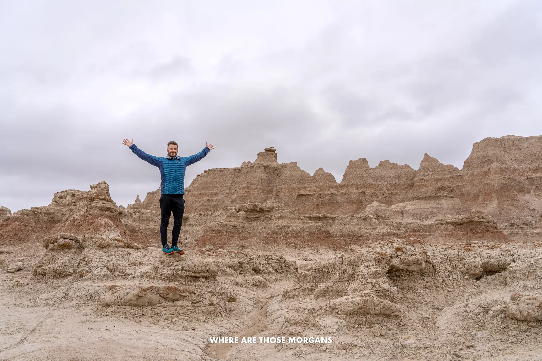 Mark from Where Are Those Morgans standing in a rocky landscape holding arms in the air with no people around and a very cloudy sky