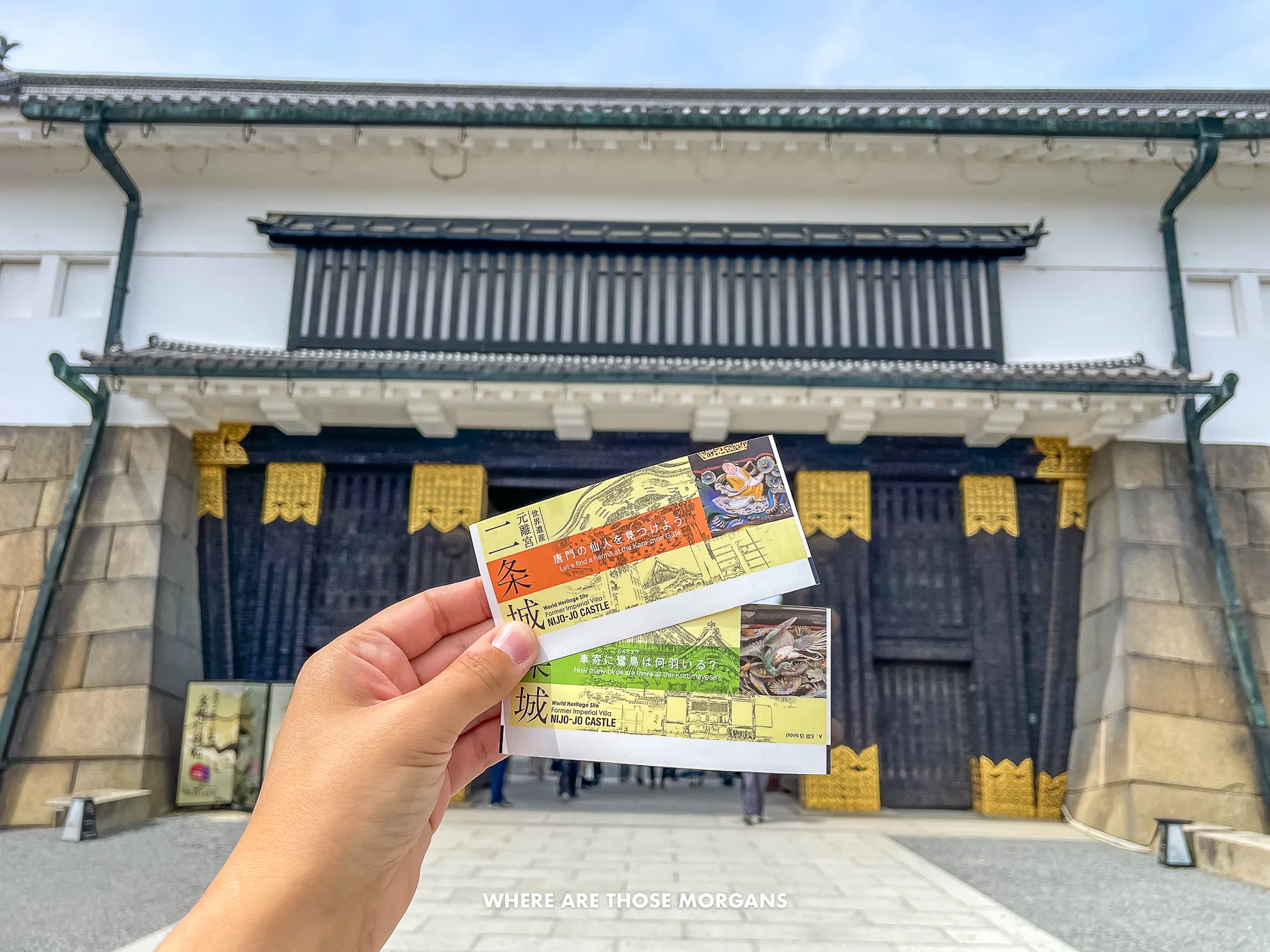 Hand holding tickets in front of a gate entrance to a castle in Japan
