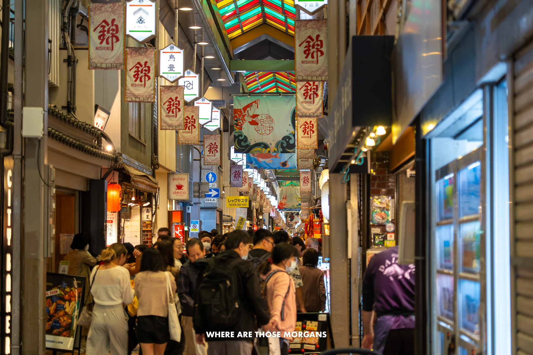 Tall but narrow pedestrian walkway through Nishiki Market in Kyoto with tourists crammed in-between food stalls