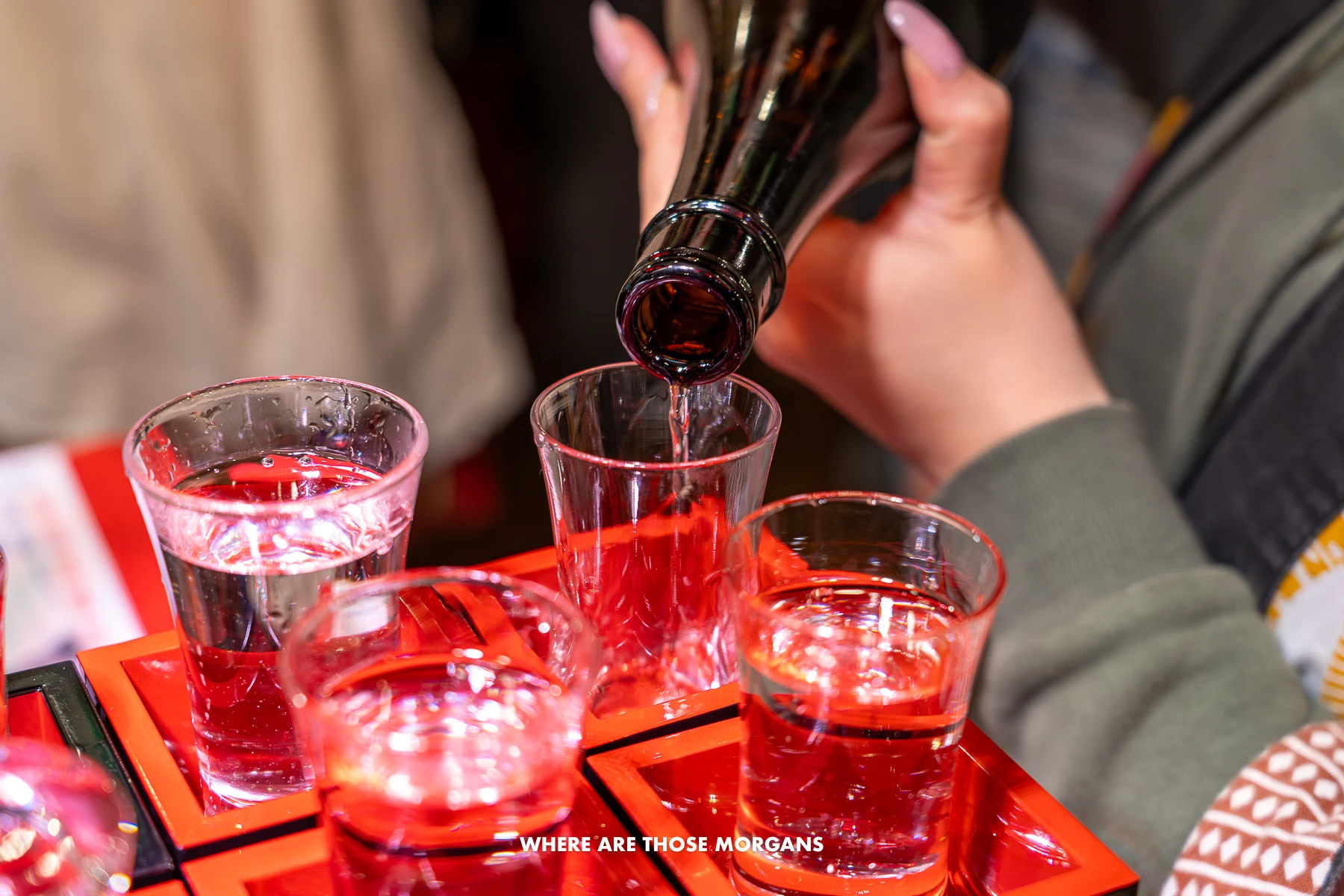 Red tray with small shot glasses being filled with sake in Japan