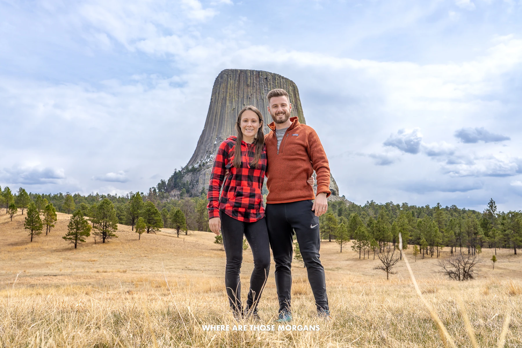 Mark and Kristen from Where Are Those Morgans standing together in front of Devils Tower National Monument from a middle distance viewpoint in a prarie