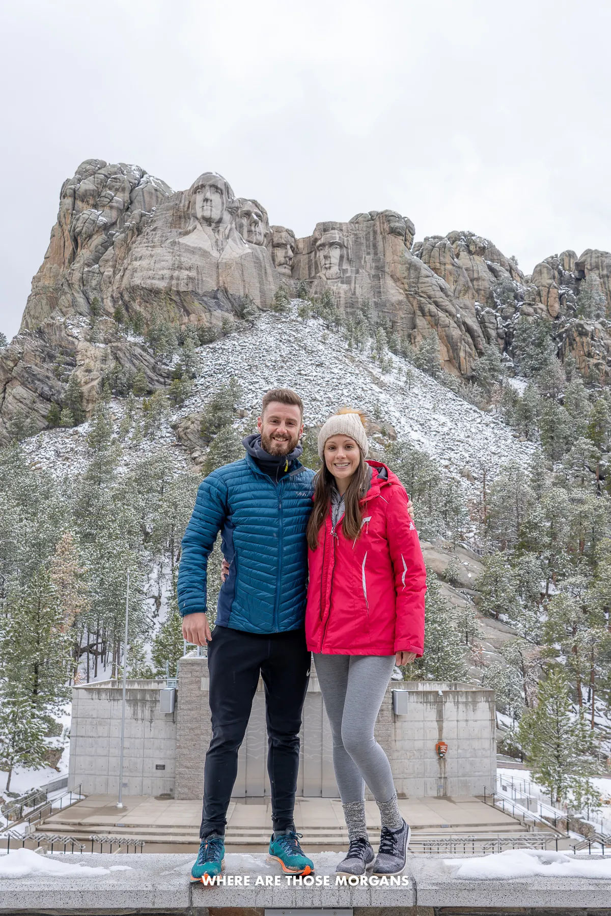 Mark and Kristen from Where Are Those Morgans standing together for a photo in the amphitheater with Mount Rushmore behind and above