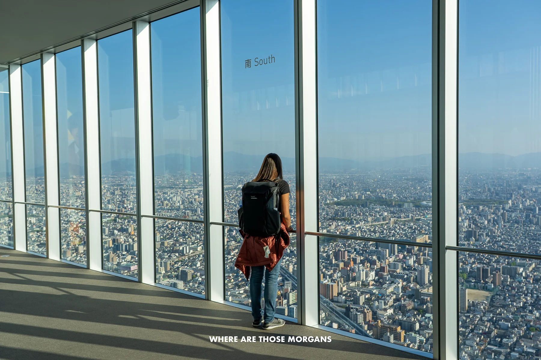 Kristen from Where Are Those Morgans looking out of tall glass windows at the city of Osaka on a clear sunny day