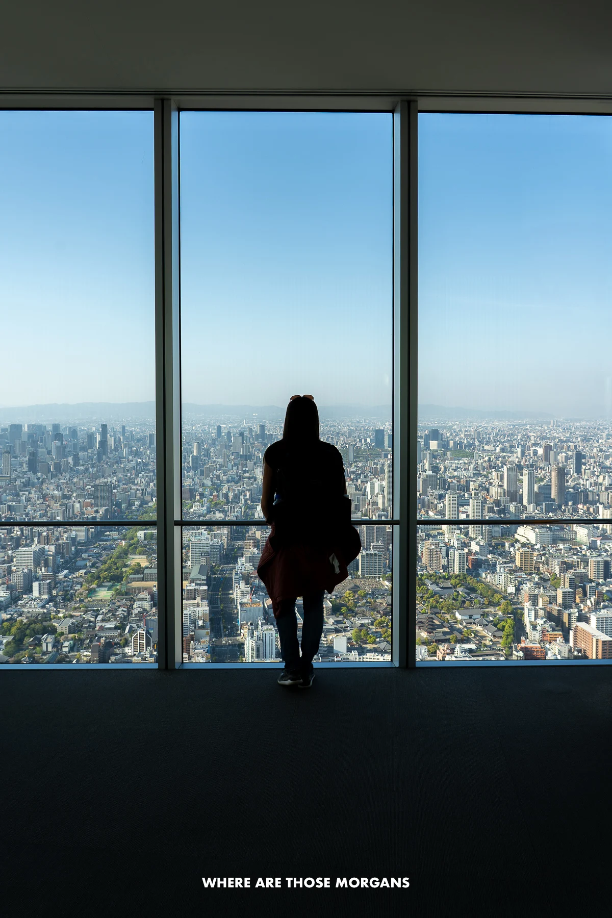 Kristen from Where Are Those Morgans silhouetted against a ceiling to floor window looking out over the city of Osaka