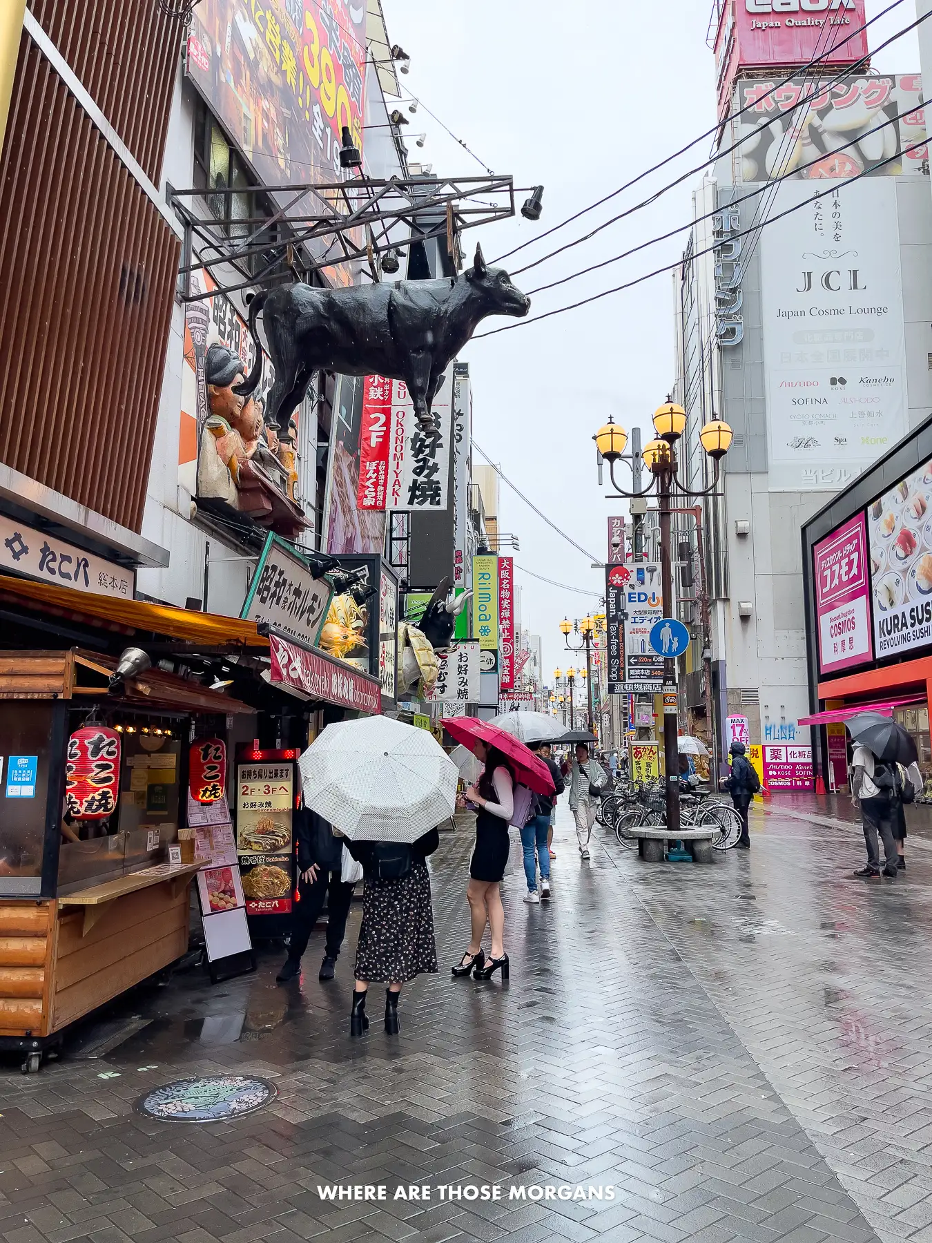 People with umbrellas walking down a street with over the top restaurant facades in Osaka