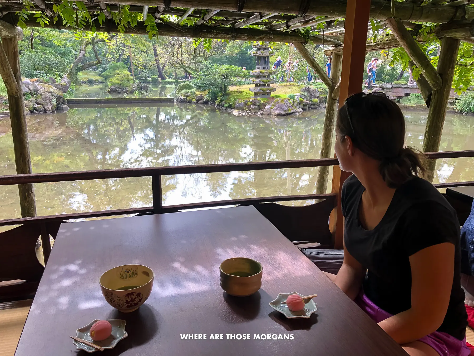 Kristen from Where Are Those Morgans sat on the floor with a low table holding two matcha teas with views out to a pond inside a garden in Kanazawa Japan
