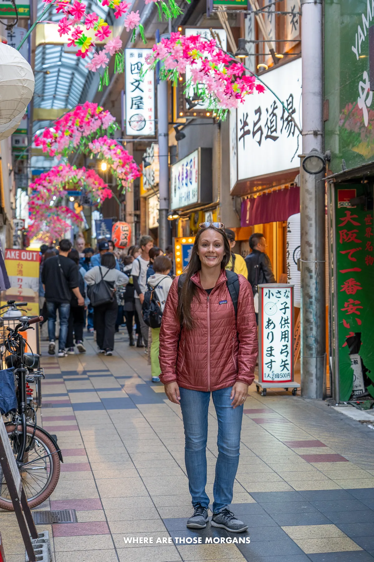 Kristen from Where Are Those Morgans walking through a covered shopping arcade in Japan with other people walking by shops and restaurants behind