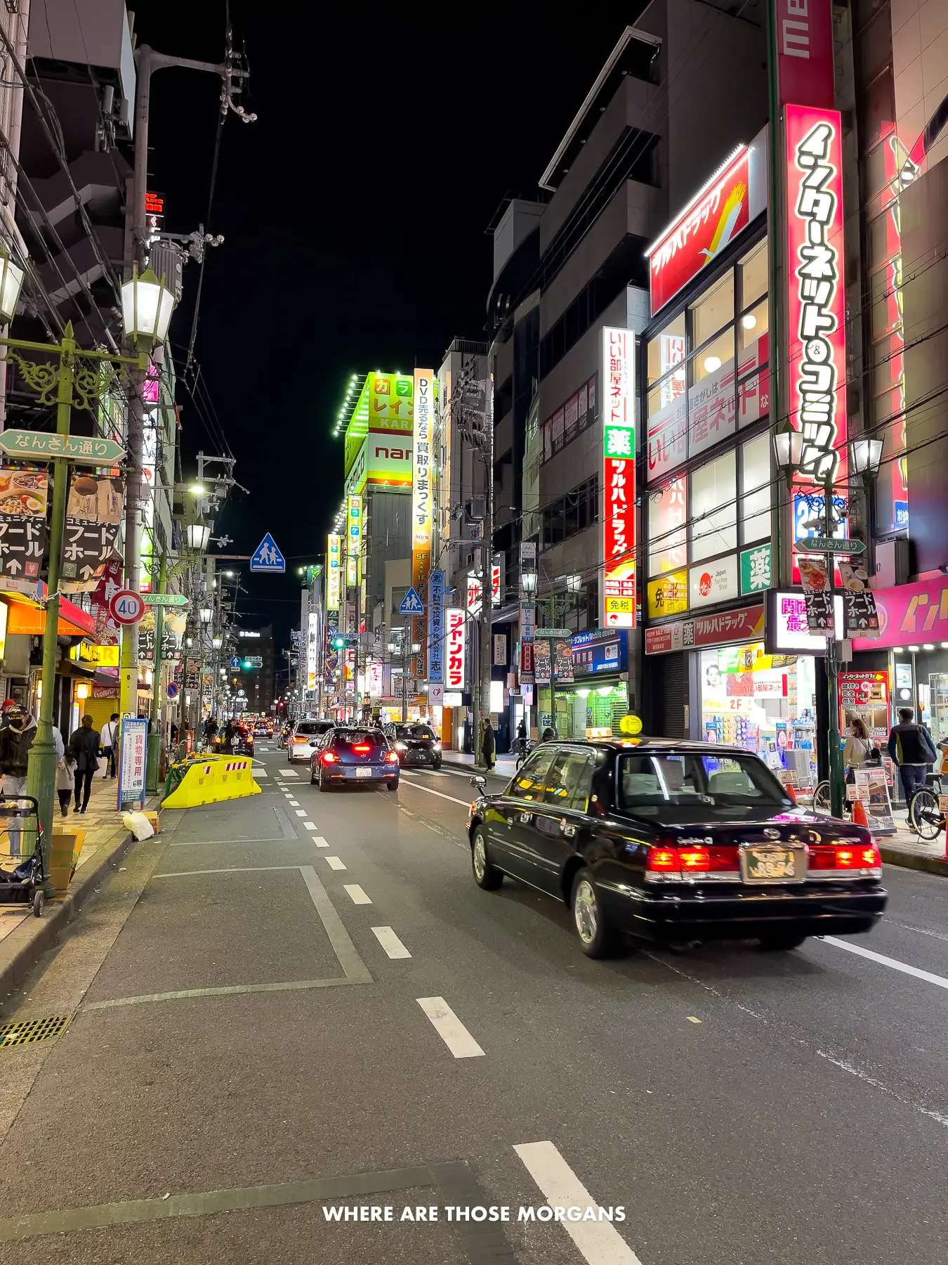Cars and people passing between neon-lit buildings at night in Japan