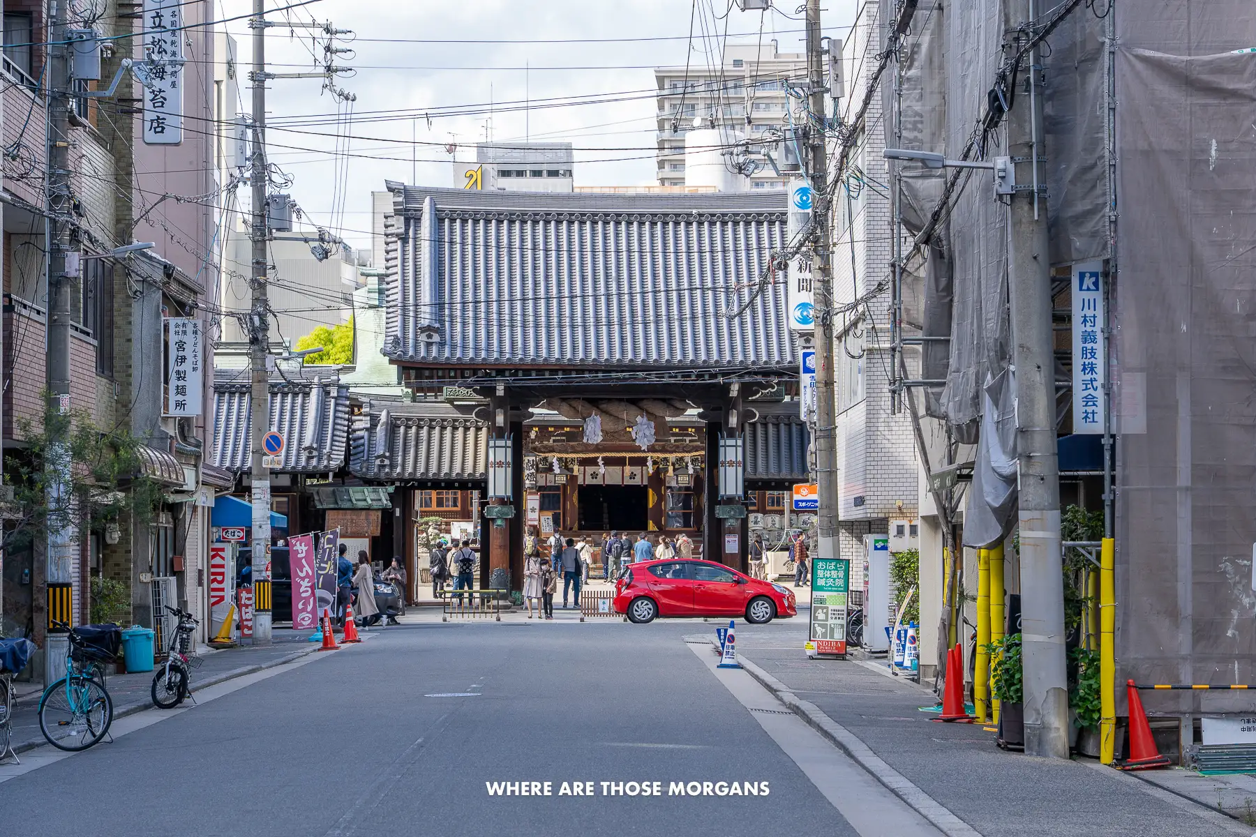 Looking up a street in Osaka at the entrance to Tenmangu Shrine with people and cars on the street