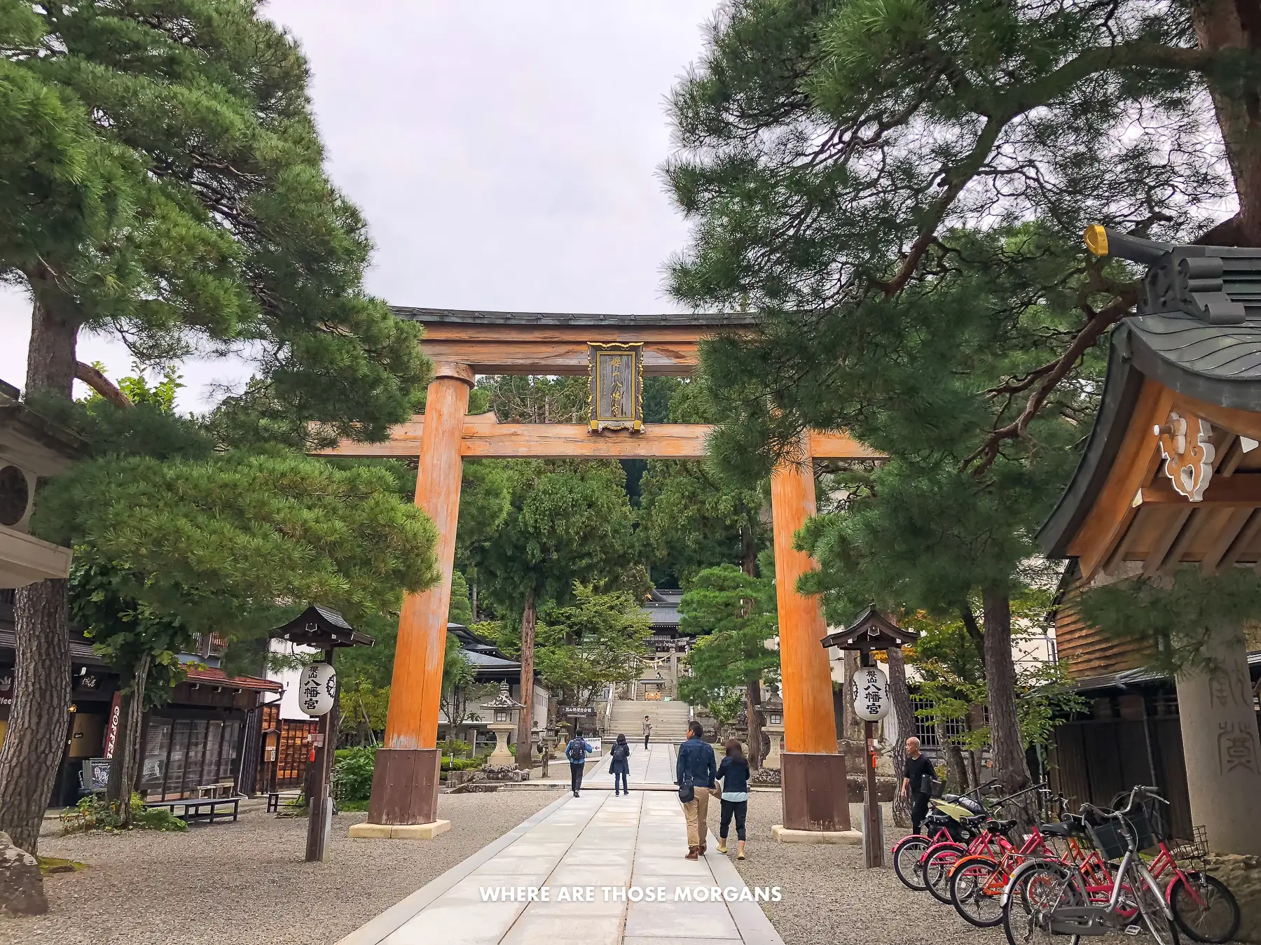 Giant orange torii gate leading to a wooden shrine surrounded by trees in Takayama