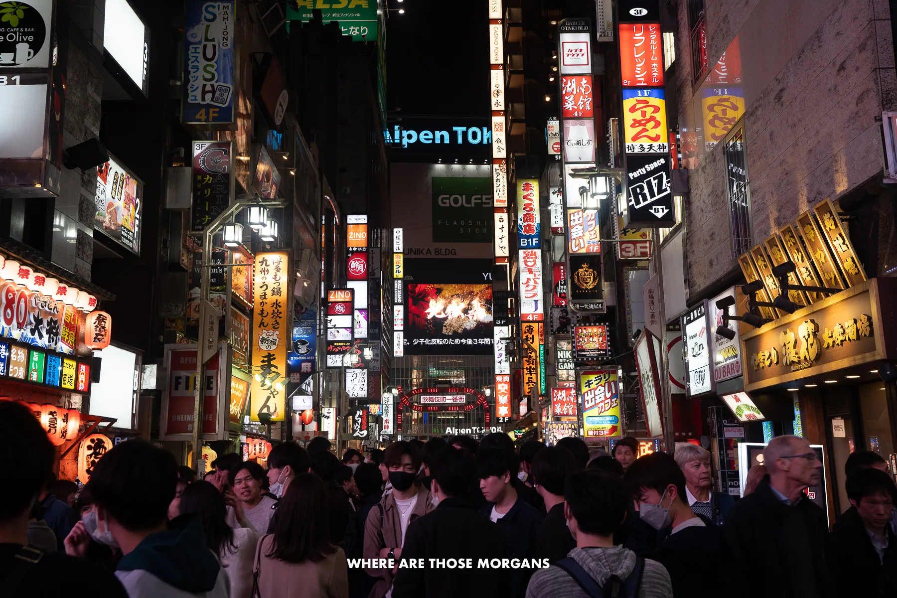 Dense crowd of people walking down a neon-lit street at night in Tokyo