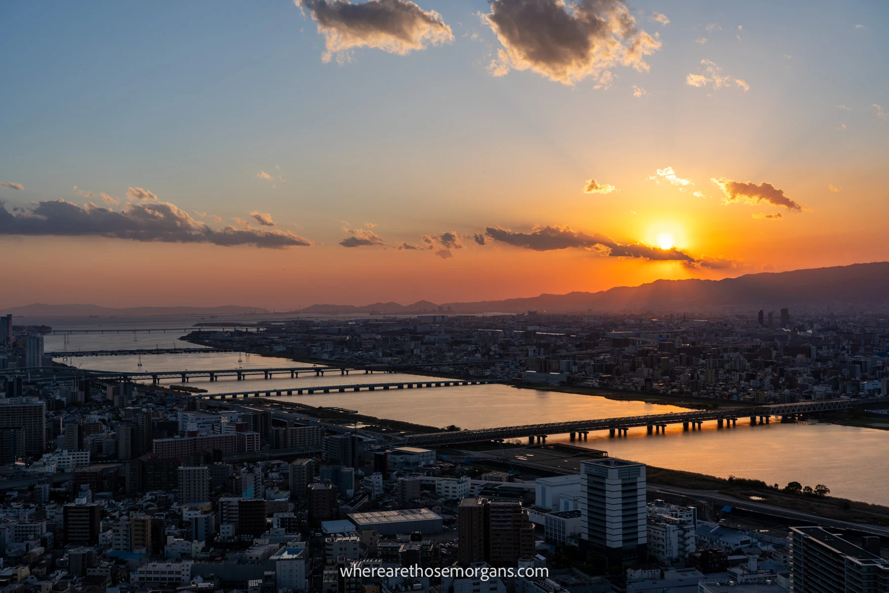 Serene sunset over a city with bridges crossing a river and distant low mountains in Japan