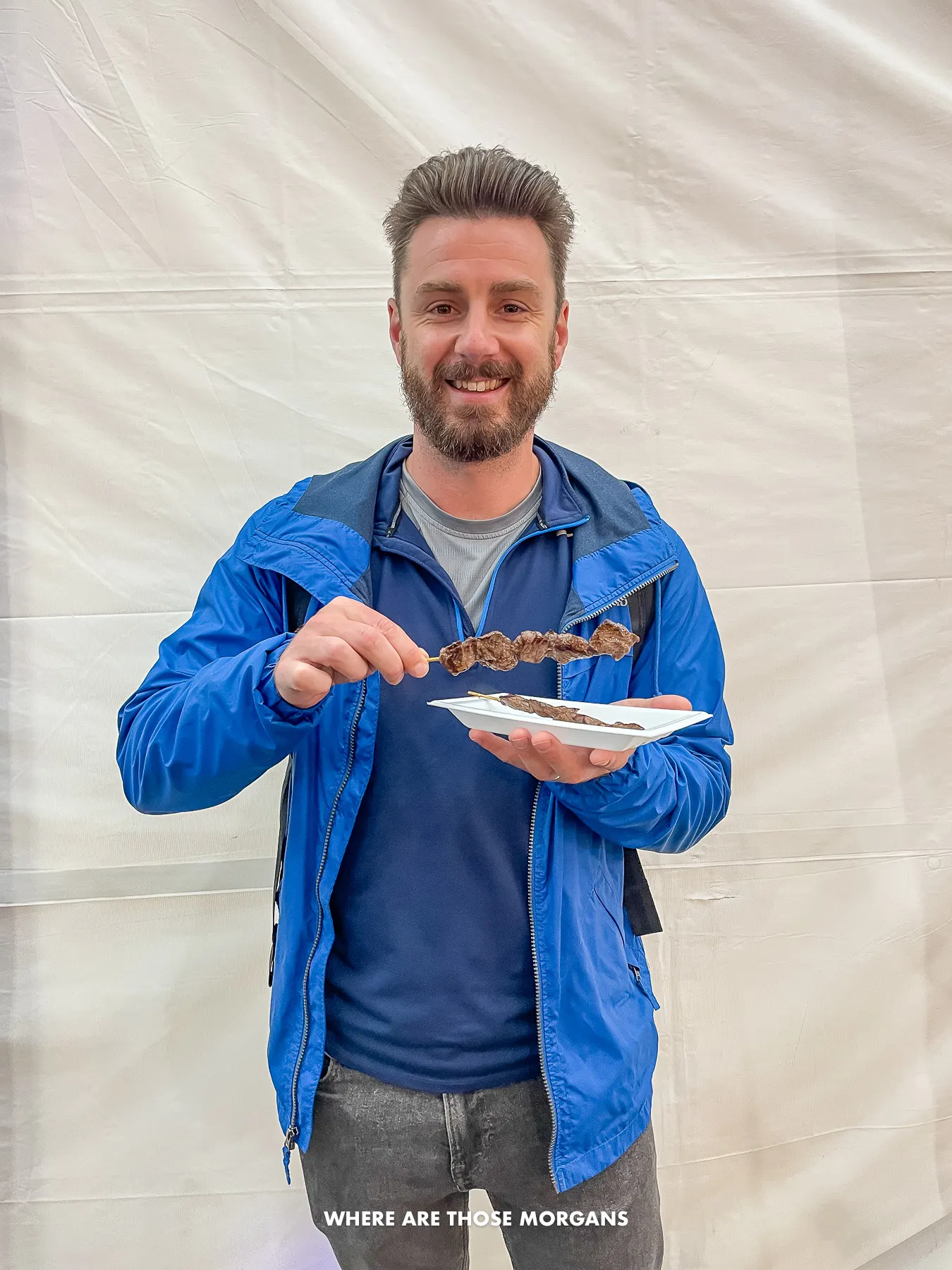 Mark from Where Are Those Morgans standing inside a market holding a plate full of beef skewers in Osaka