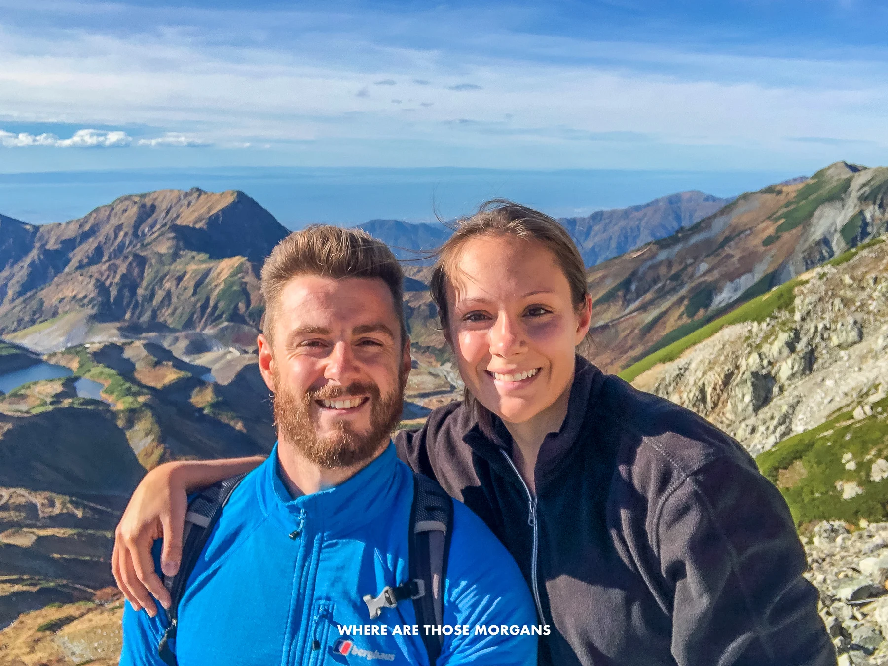 Mark and Kristen from Where Are Those Morgans taking a selfie at the top of Mt Oyama in the Japanese Alps with wide open views of mountains and the distant ocean behind