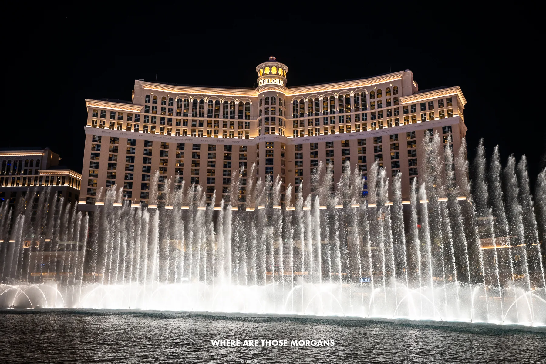 Photo of the Bellagio Fountains in full display with jets of water shooting up to contrast against the hotel lit up and the dark night sky