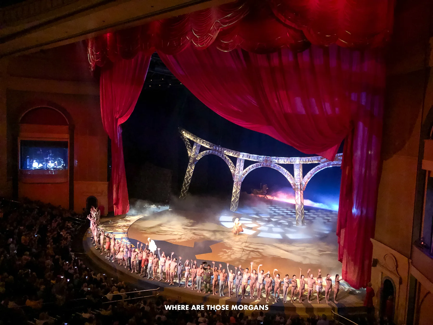Massive stage with red curtains and the cast of a show lined up for a bow after the performance