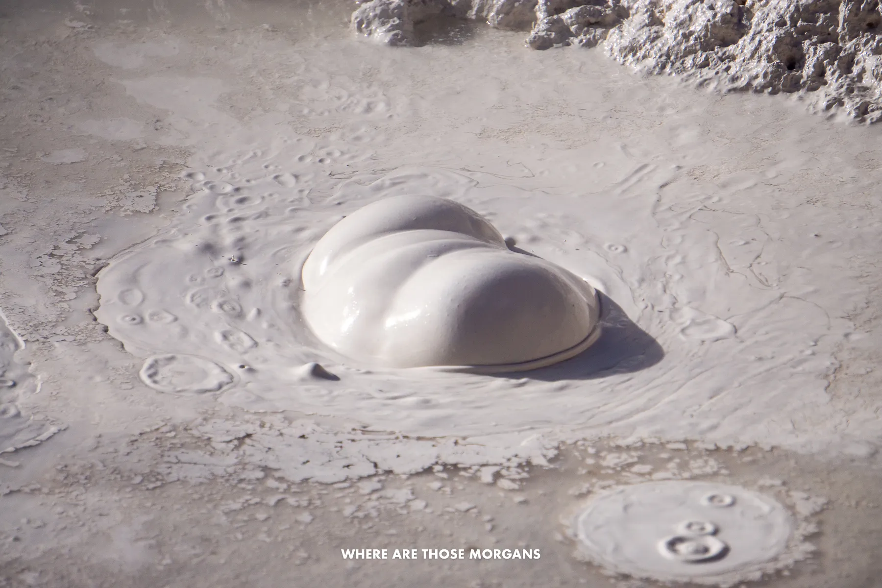Massive bubbling mud pot in Yellowstone National Park with three joining bubbles in the middle blowing up