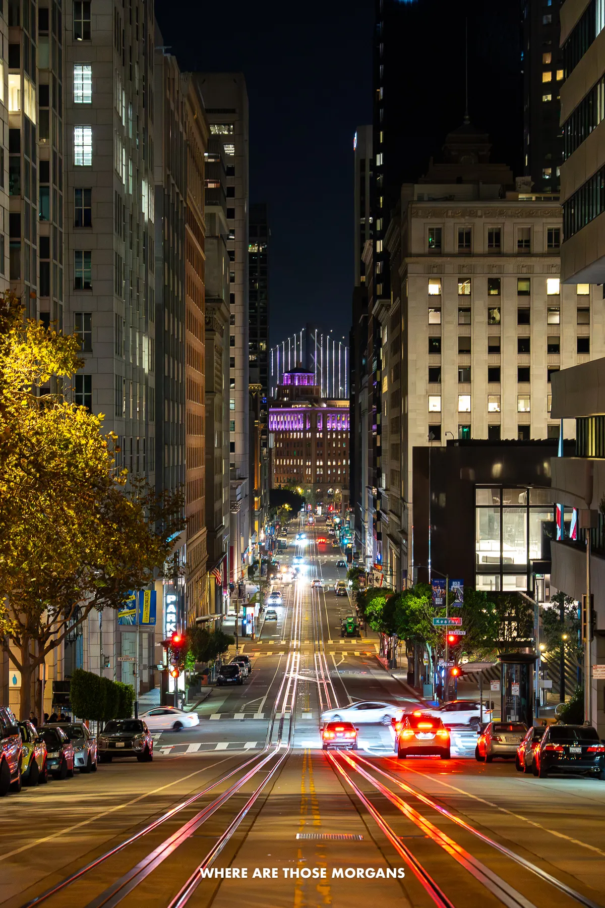 San Francisco street at night with cable car tracks and a bridge illuminated in the background