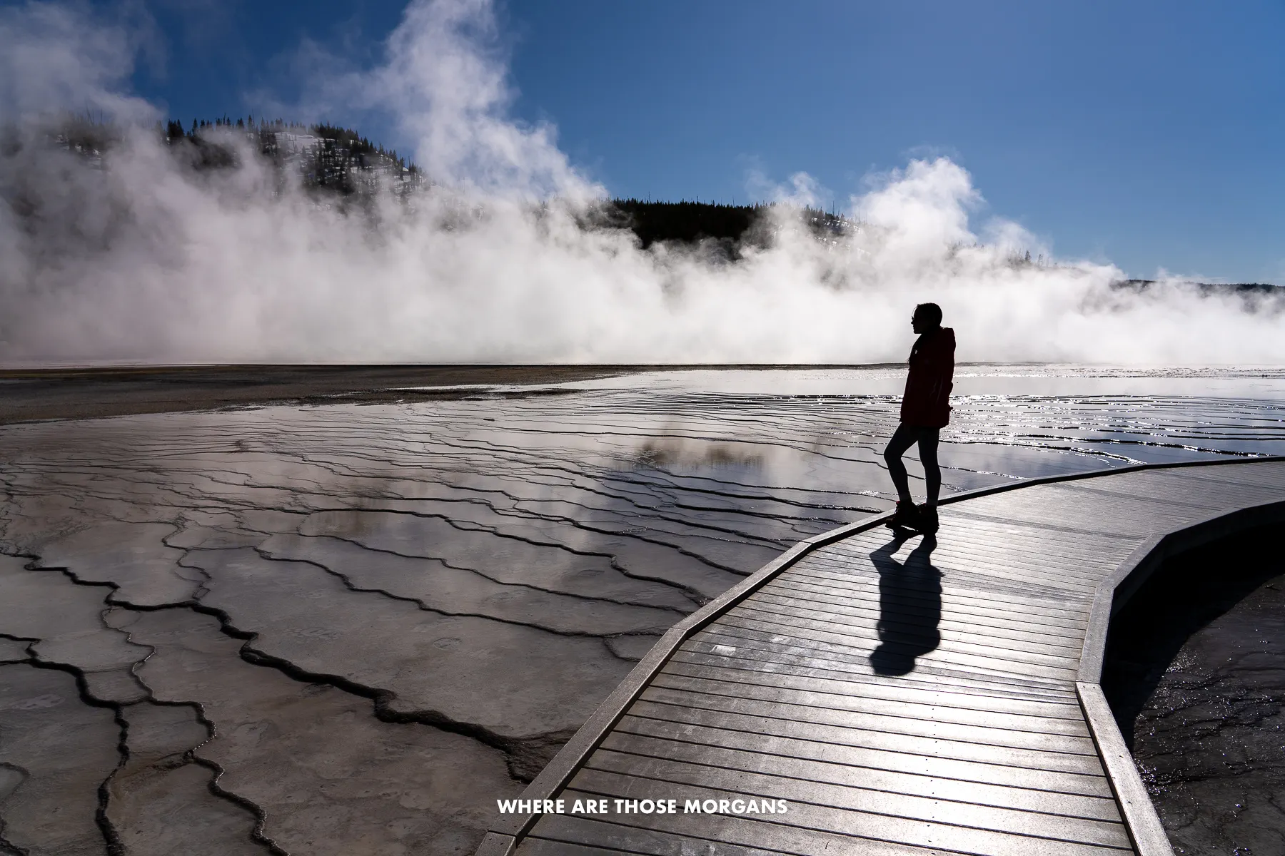 Kristen from Where Are Those Morgans walking on the wooden boardwalk at Grand Prismatic Spring with steam lighting up under the sun