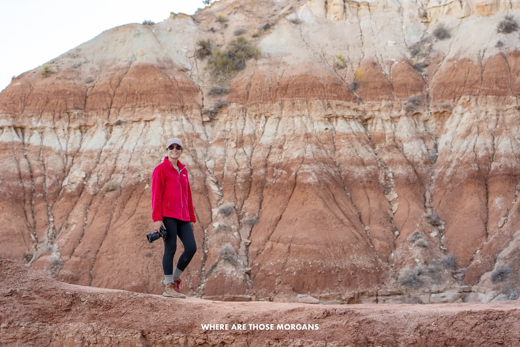 Kristen from Where Are Those Morgans hiking along a red and white rocky ledge holding a camera in southern Utah