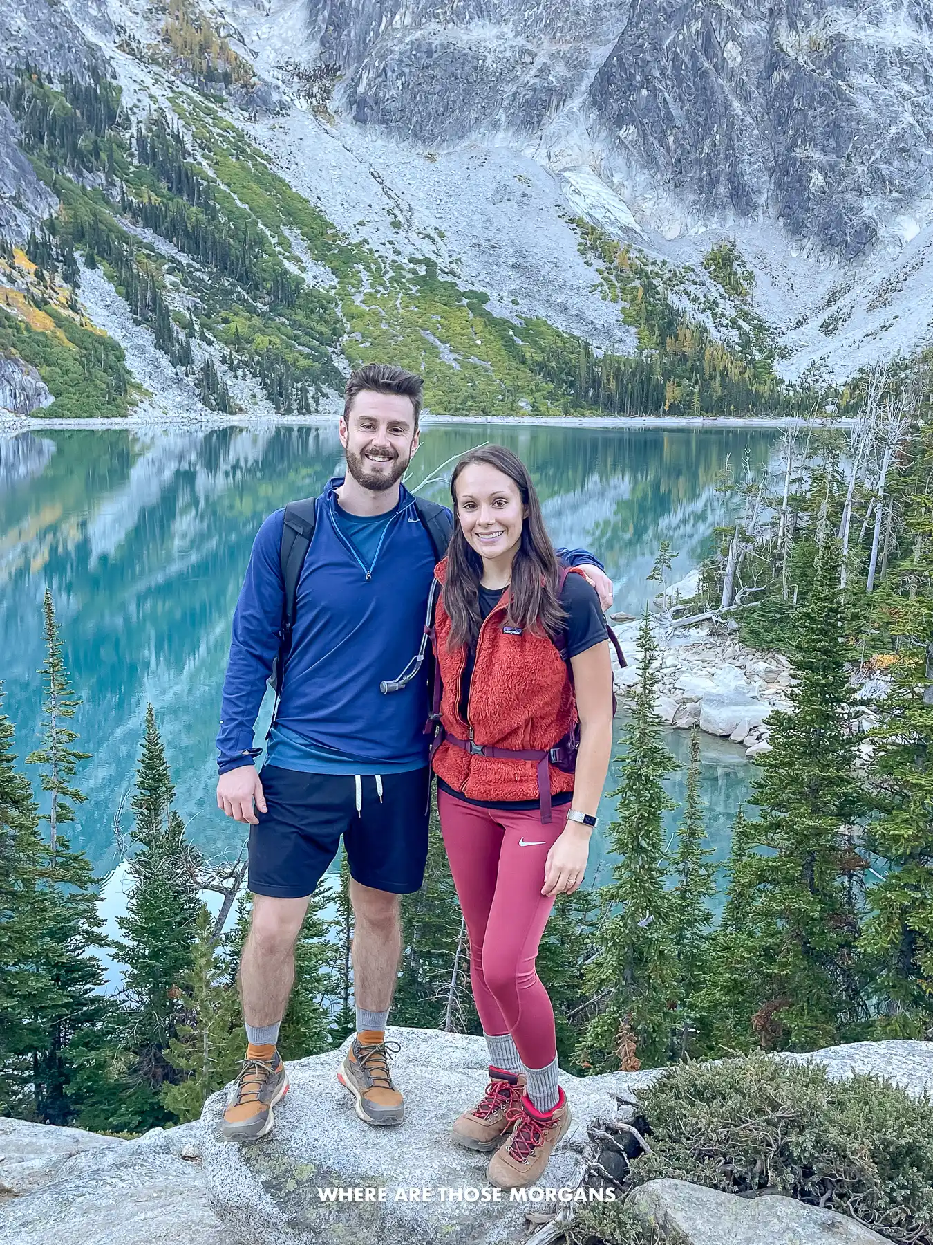 Mark and Kristen from Where Are Those Morgans standing together for a photo on a rock with Colchuck Lake and Aasgard Pass behind on The Enchantments Trail
