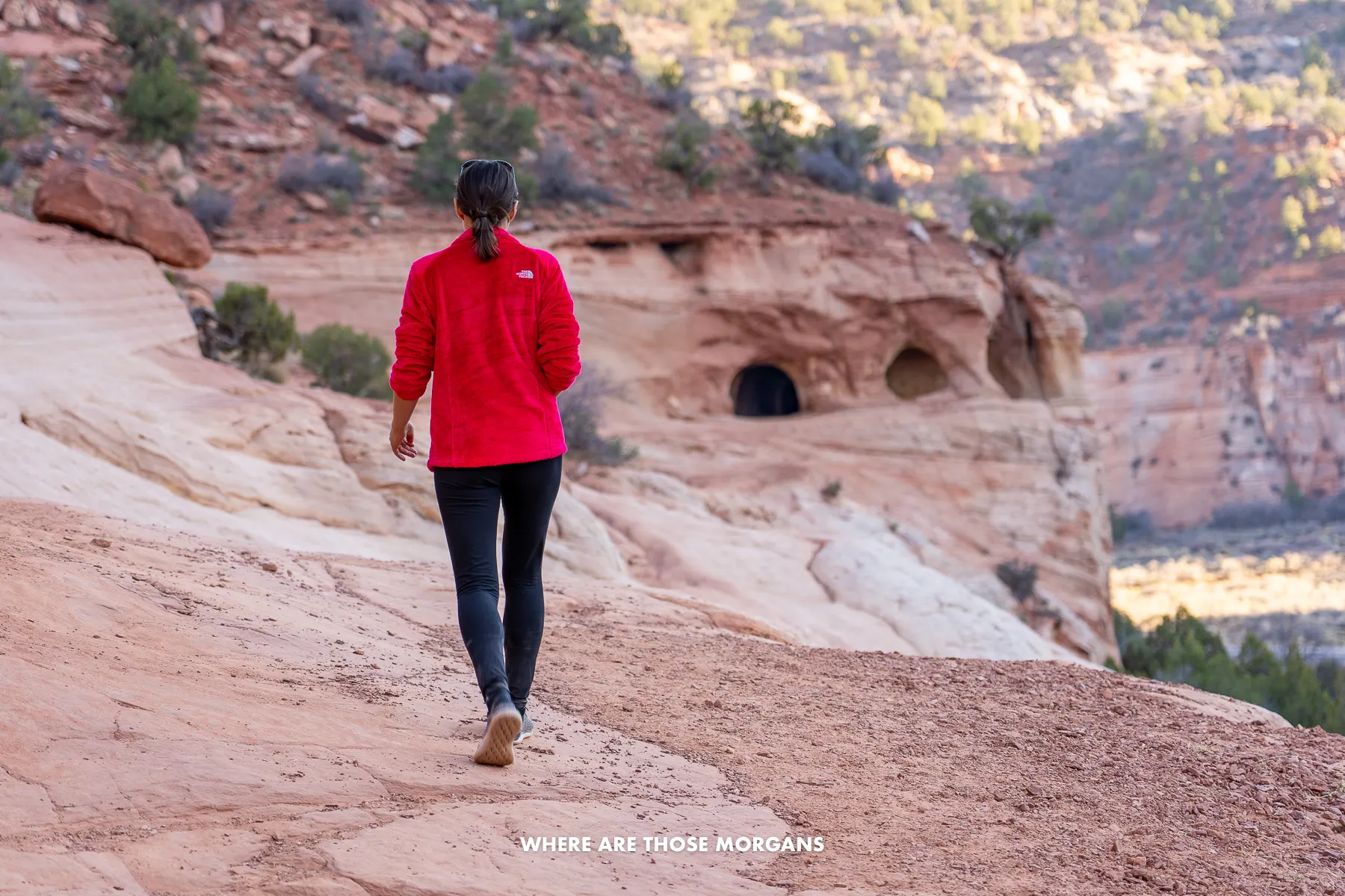 Kristen from Where Are Those Morgans hiking on a rocky ledge towards small cave openings near Kanab
