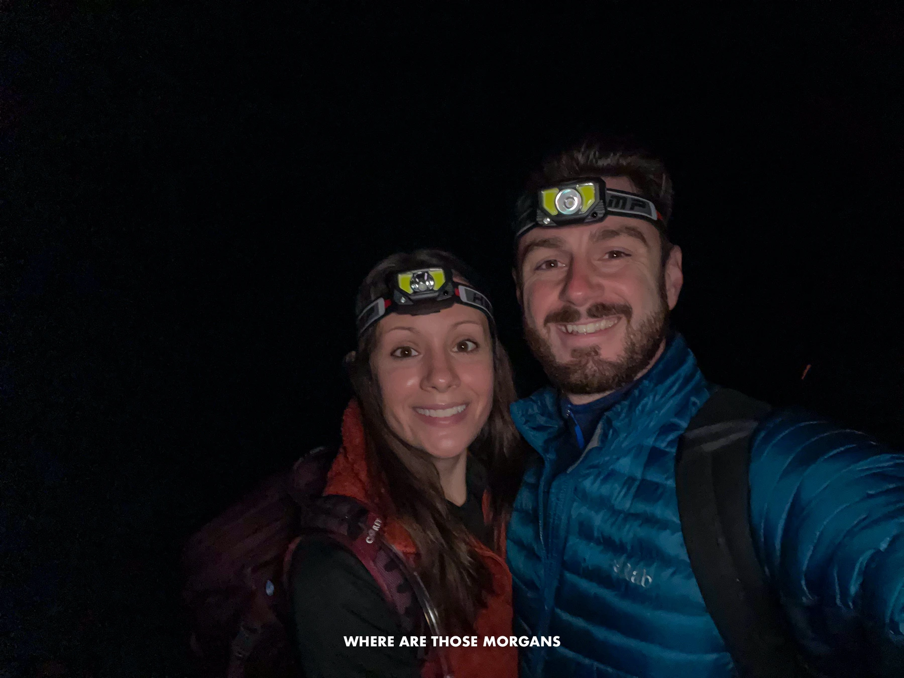 Mark and Kristen from Where Are Those Morgans taking a selfie in total darkness wearing coats and headlamps at the start of a thru hike to The Enchantments in Washington