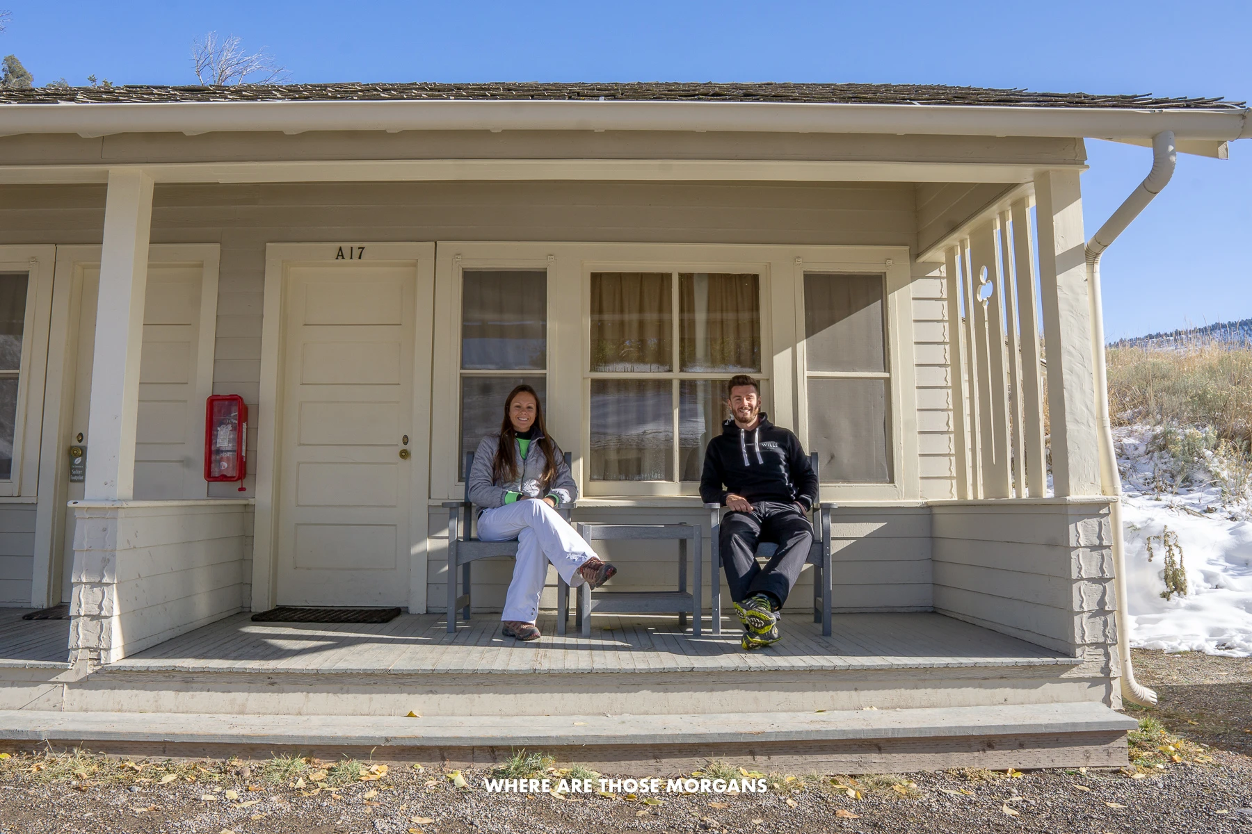 Mark and Kristen from Where Are Those Morgans sitting on chairs on a ground floor balcony outside a frontier cabin in Yellowstone National Park's Mammoth region