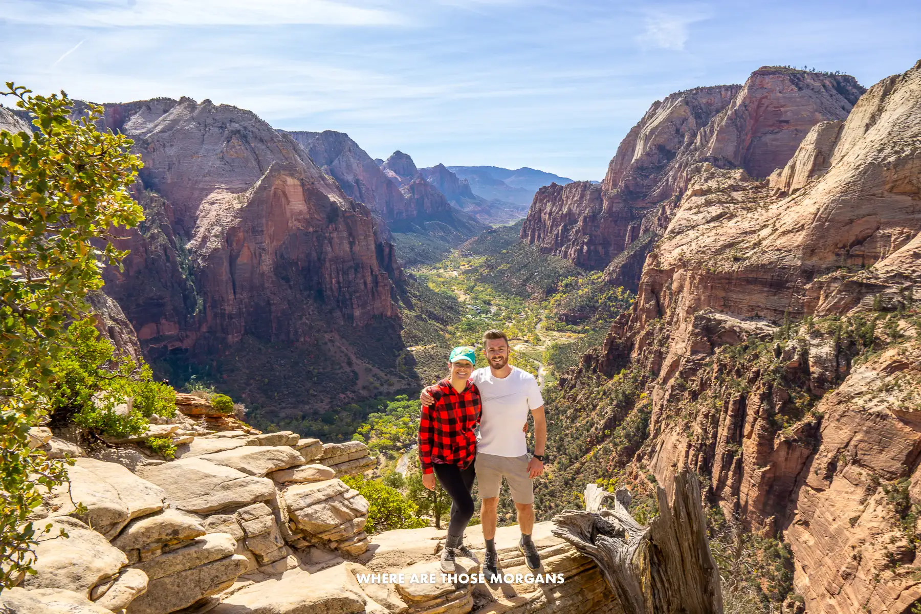 Mark and Kristen from Where Are Those Morgans standing together at the top of Angels Landing in Zion on a sunny day with expansive canyon views behind