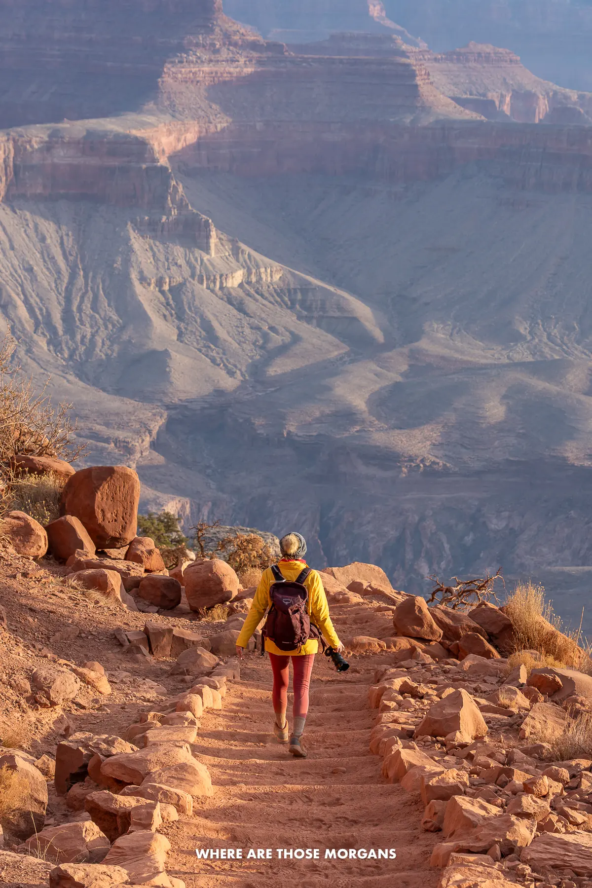 Kristen from Where Are Those Morgans hiking down a stone step path leading into the Grand Canyon on a Rim to River day hike at dawn