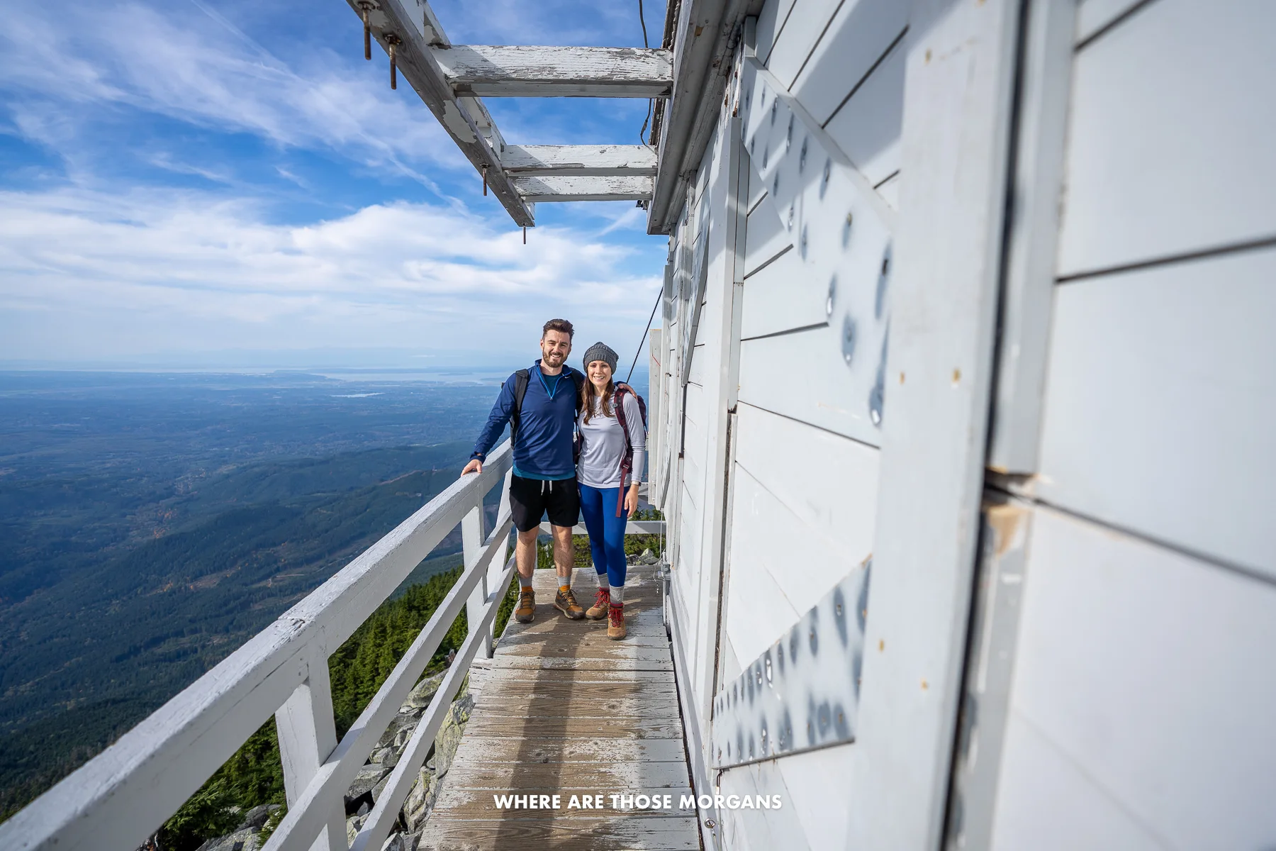 Mark and Kristen from Where Are Those Morgans standing on one side of a fire tower with views over Washington behind