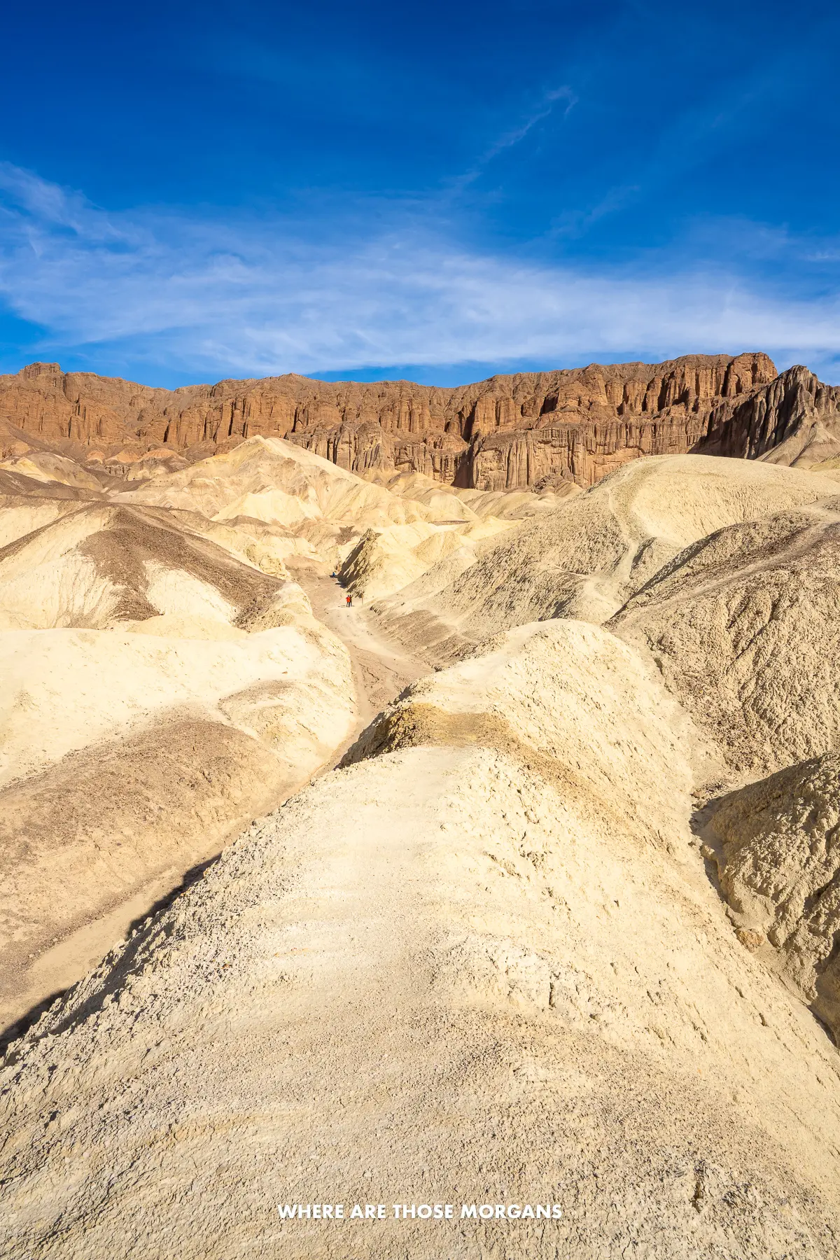 Smooth yellow colored domes in Death Valley leading to a giant red cliff under a blue sky