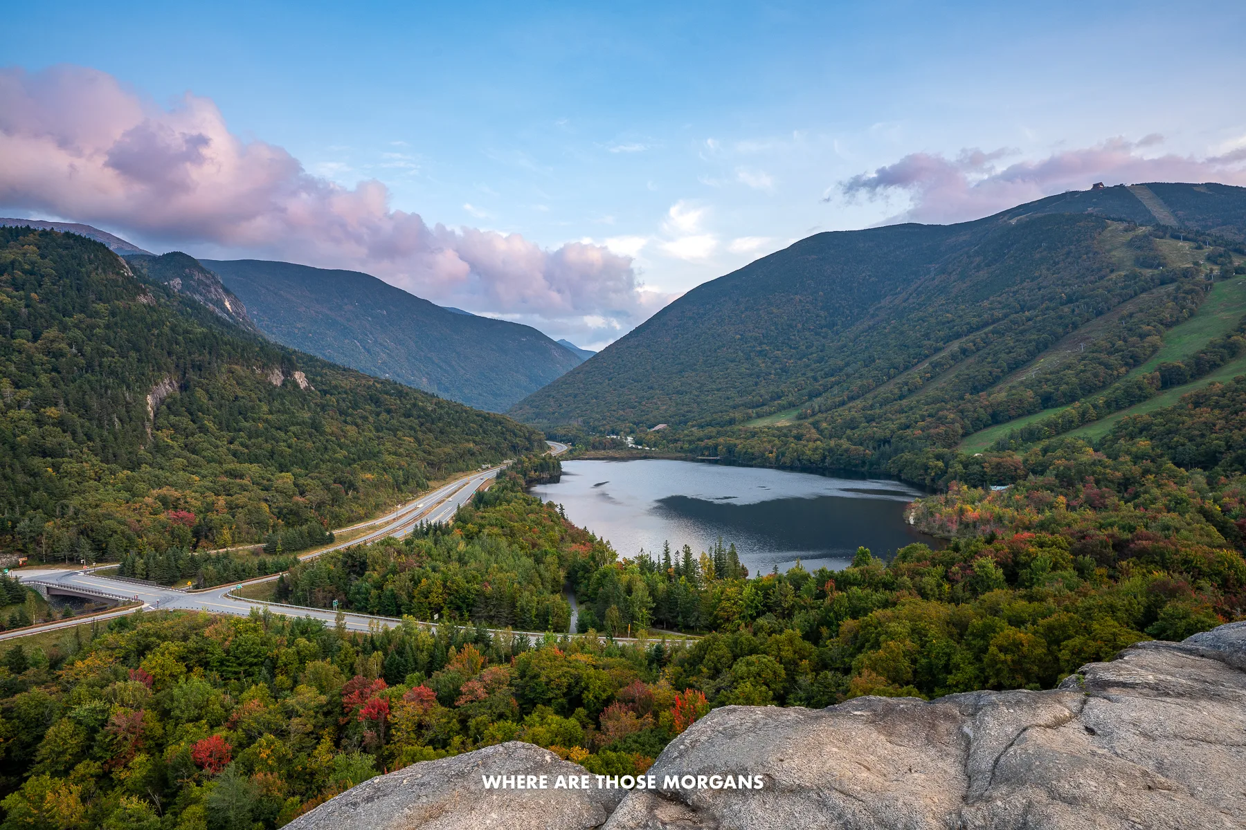 View from Artists Bluff in New Hampshire at sunset with Echo Lake below and hills covered in trees behind