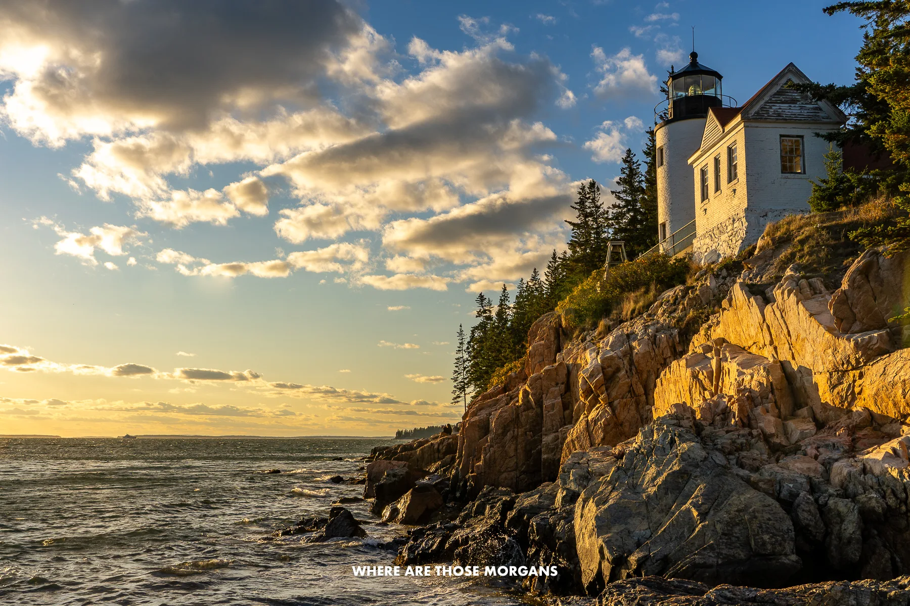 Maine coastline with rocks and a lighthouse perched on the edge of a cliff at sunset