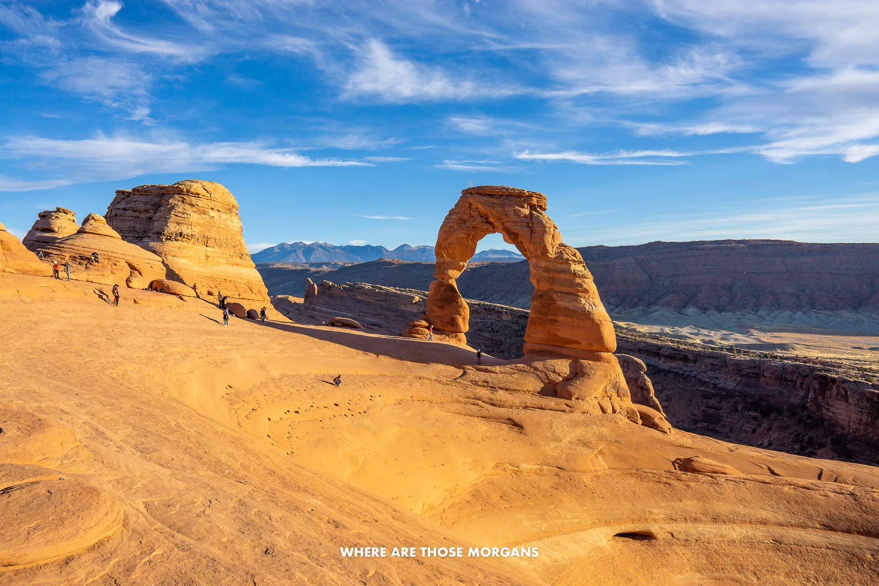 Sloping sandstone landscape with a lone natural arch bursting into a blue sky