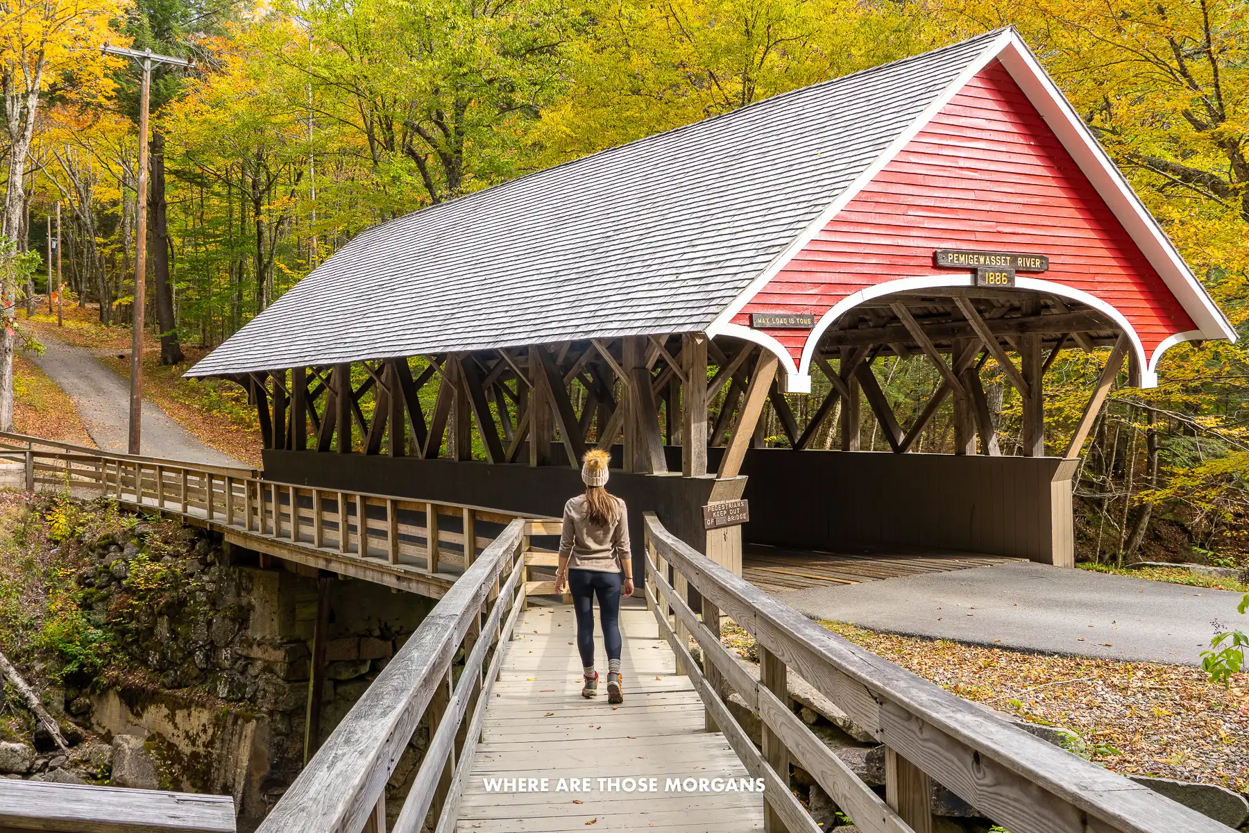 Kristen from Where Are Those Morgans walking over a wooden bridge towards a wooden covered bridge in Flume Gorge in the fall