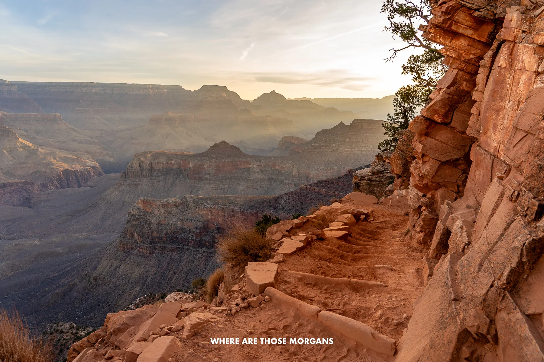 Hiking trail leading down into the Grand Canyon at sunrise with sun beams of light bursting into the canyon